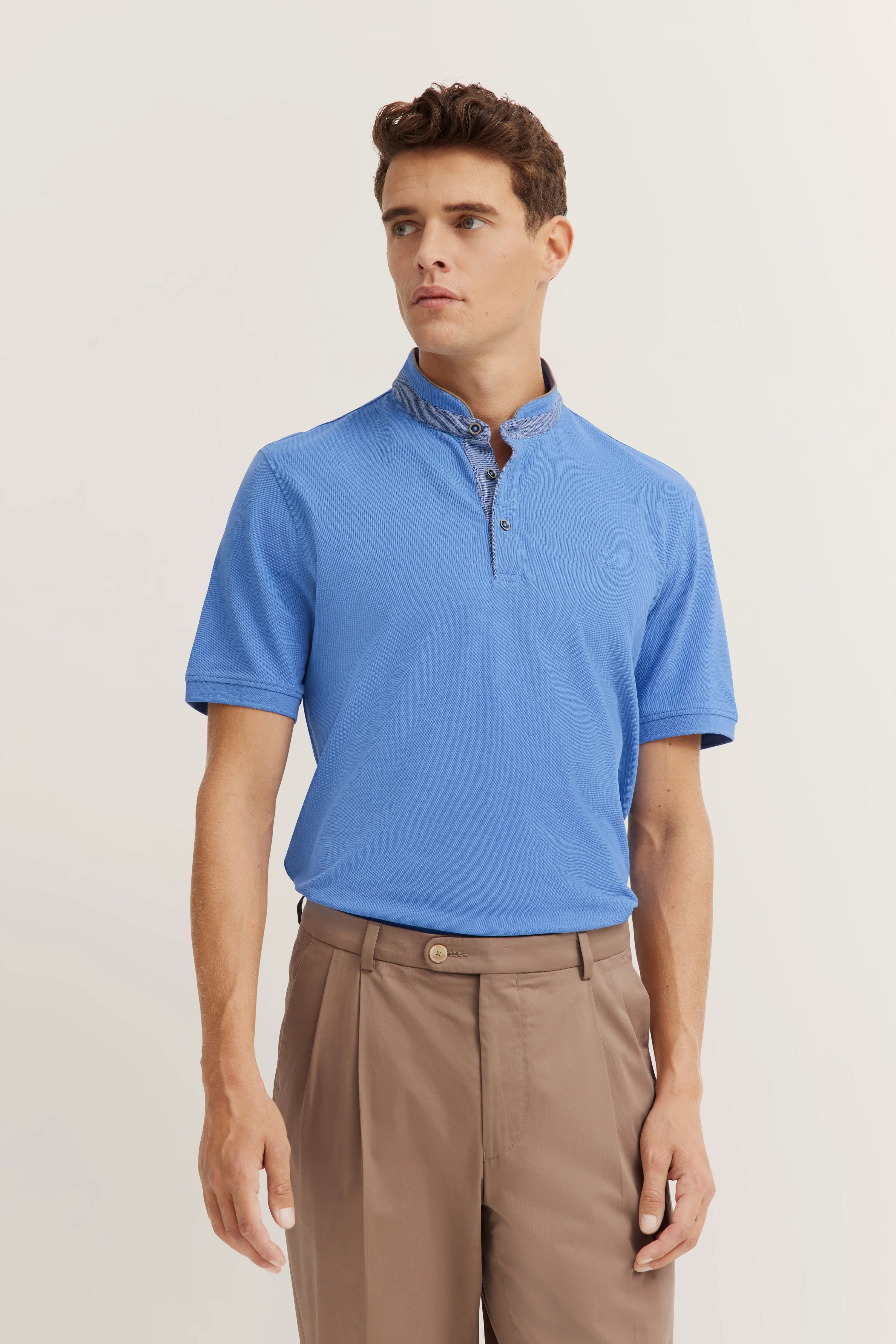 Blue polo shirt and beige pants, model in relaxed pose.