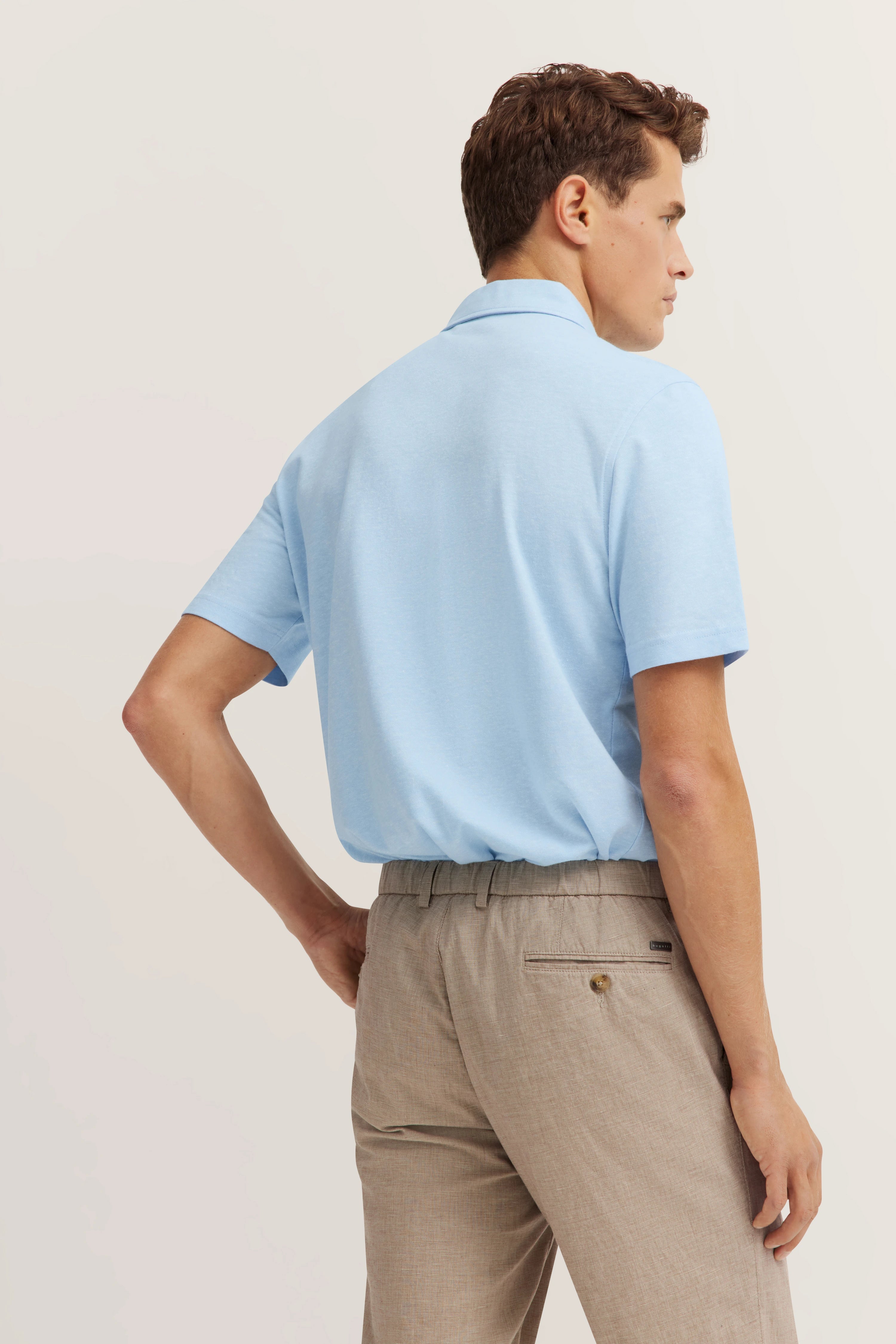 Light blue polo shirt and beige pants, model from behind, relaxed pose, bugatti style.