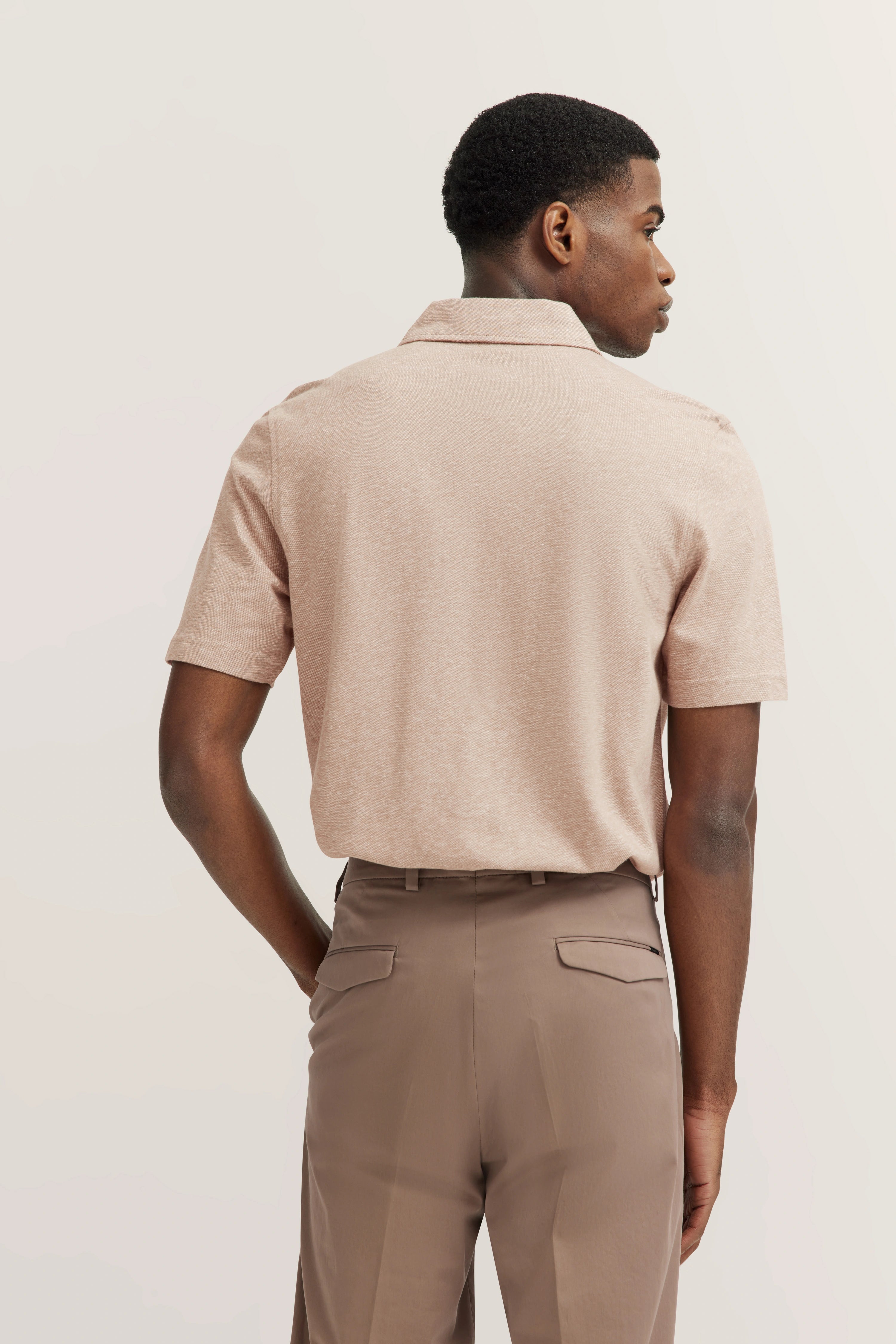 Rear view of model in beige polo shirt and brown pants, casual pose.