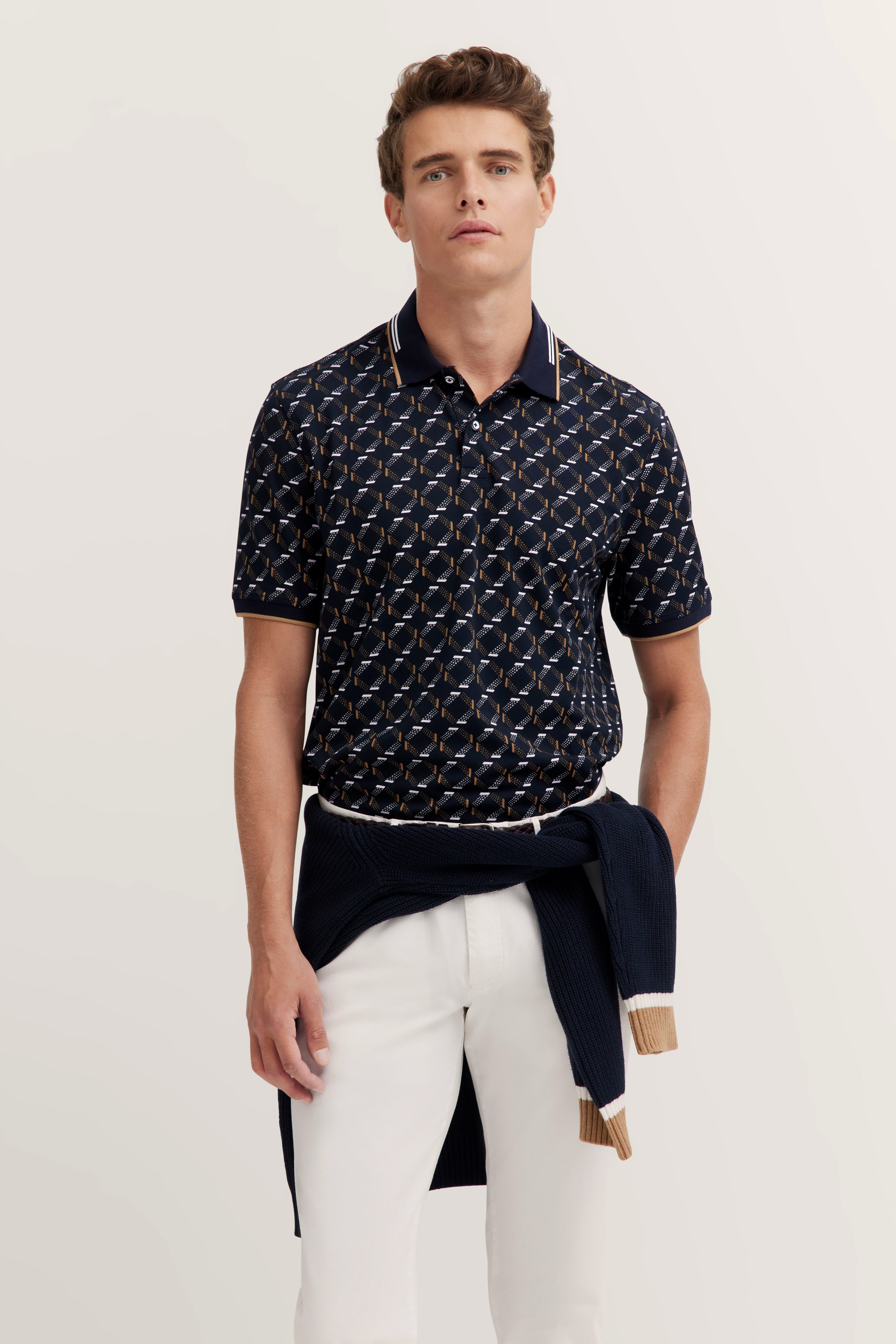 Model in patterned polo, blue sweater around waist, white pants, casual pose. bugatti style and quality.