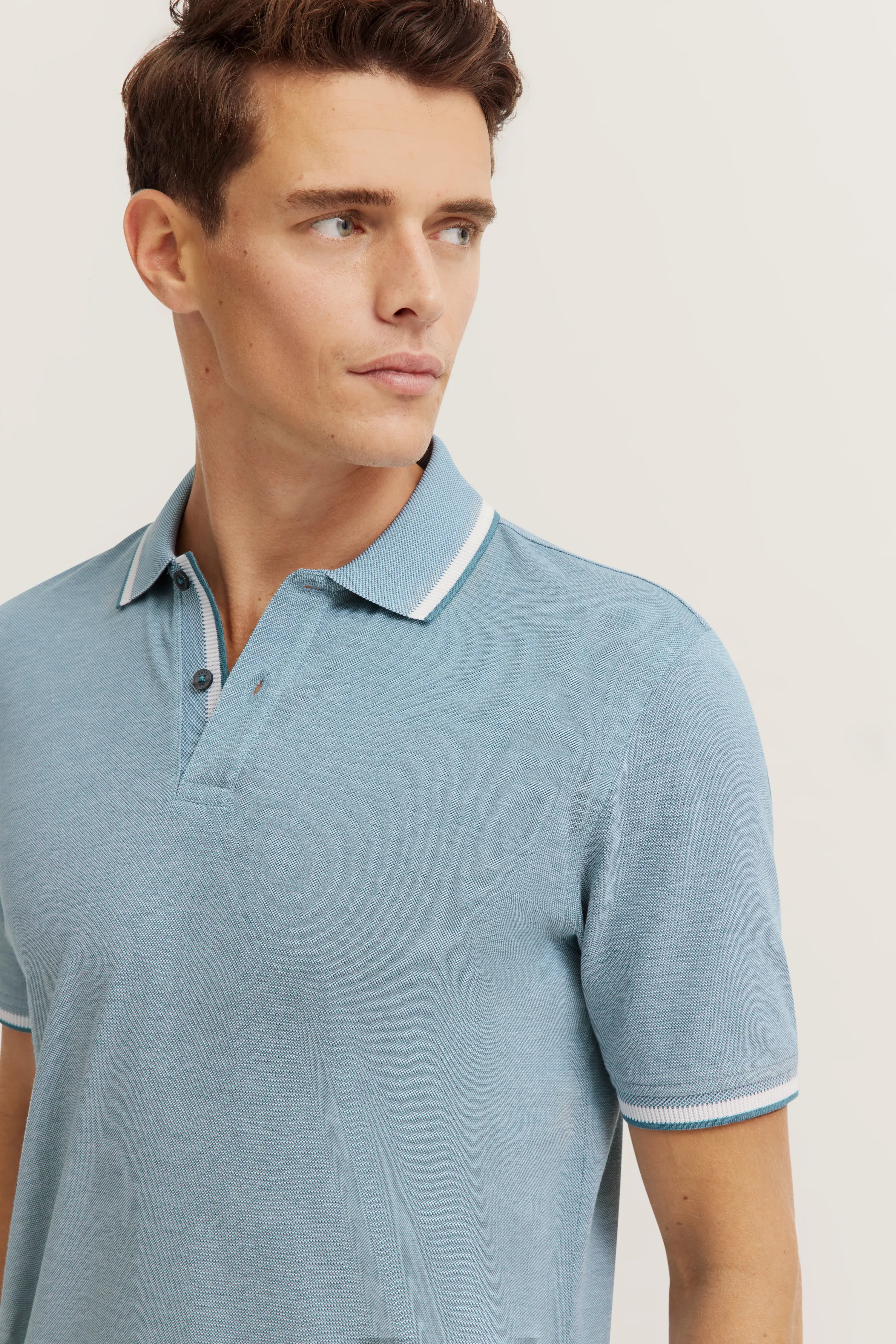 Model wears blue bugatti polo shirt, casual pose, side glance.
