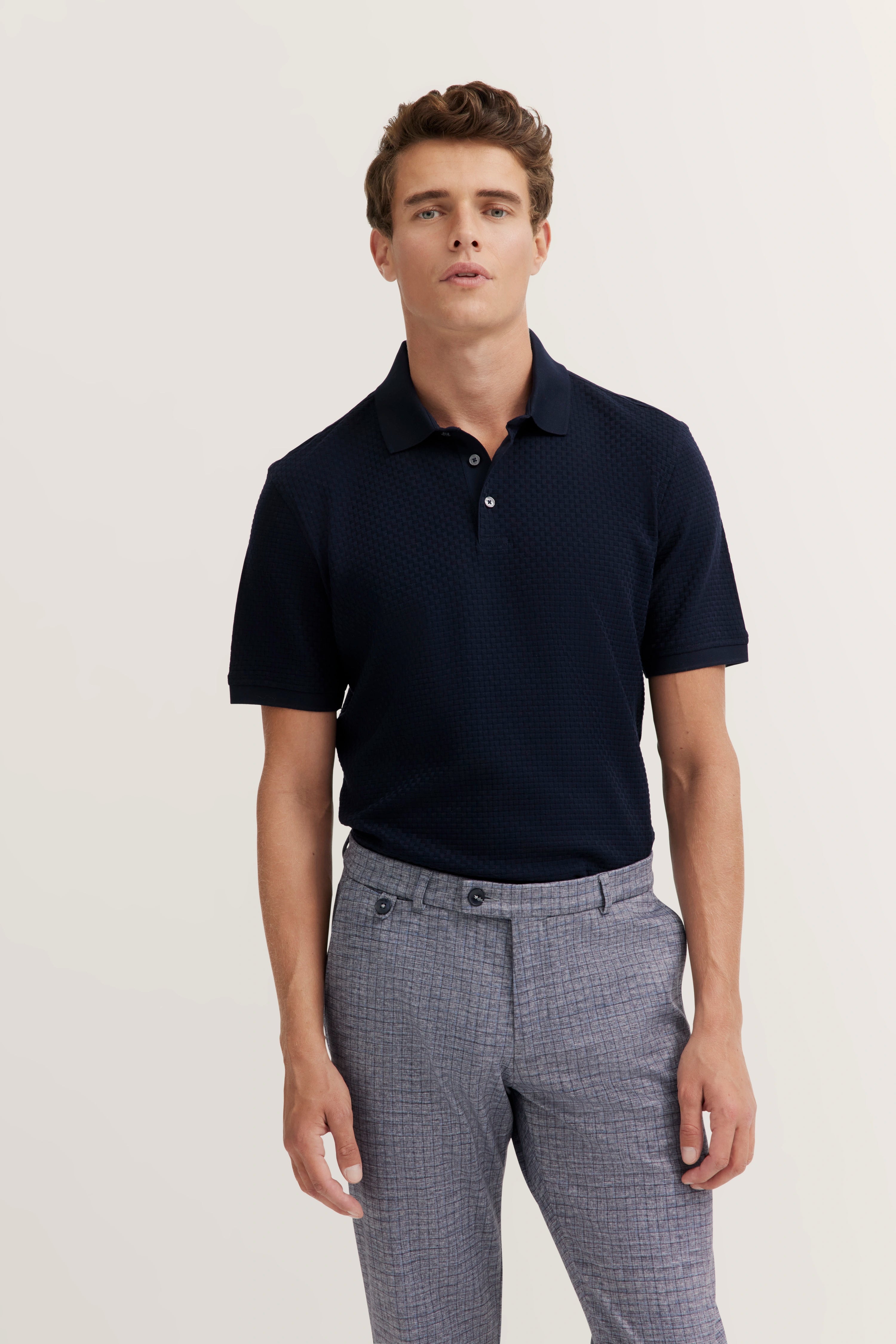 bugatti model: Dark blue polo, gray plaid pants, relaxed pose.