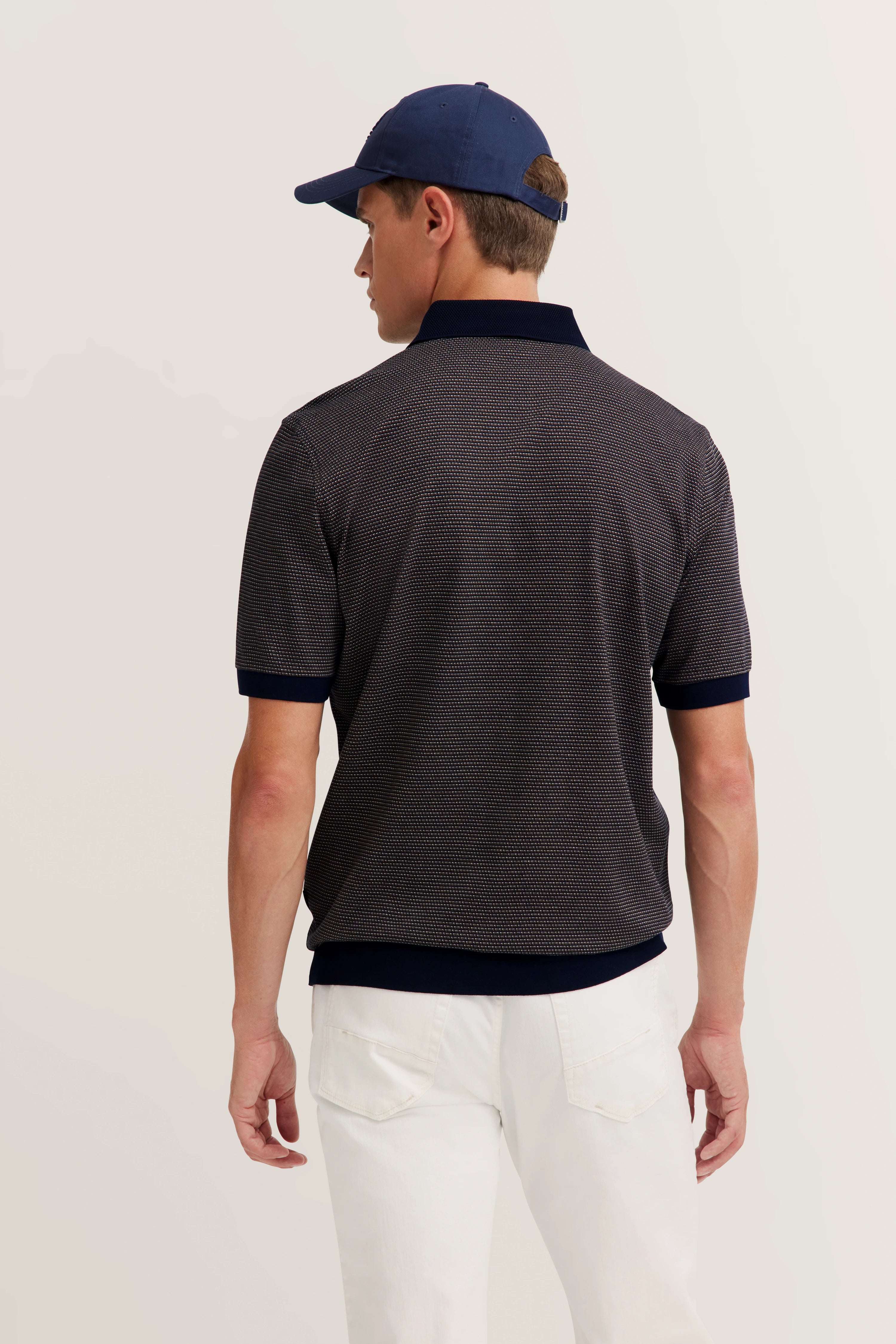 Rear view model in dark blue polo and white pants, casual pose, bugatti style.