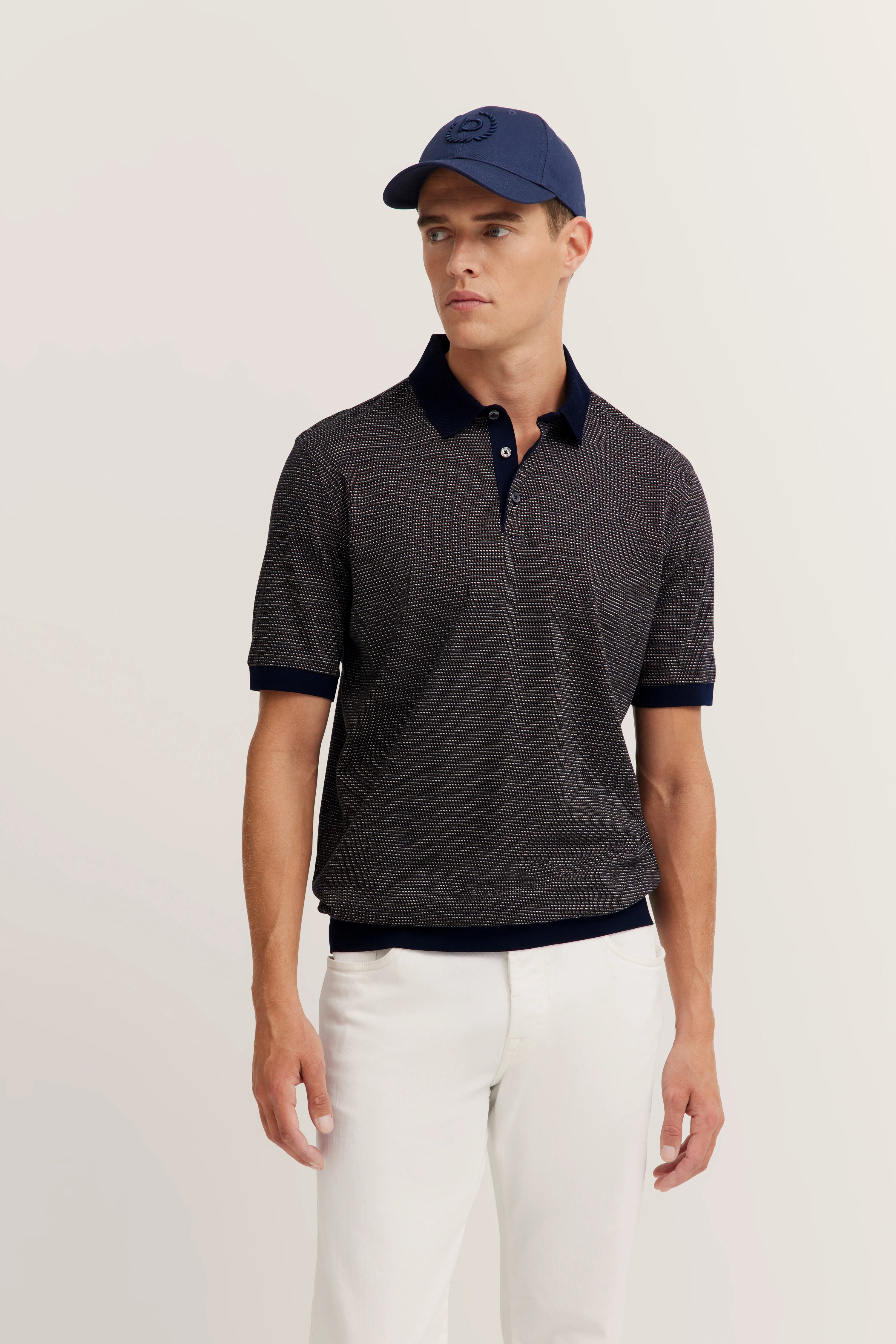 bugatti model: Man in blue polo, white pants, blue cap, relaxed pose, embodying Italian-inspired elegance and style.