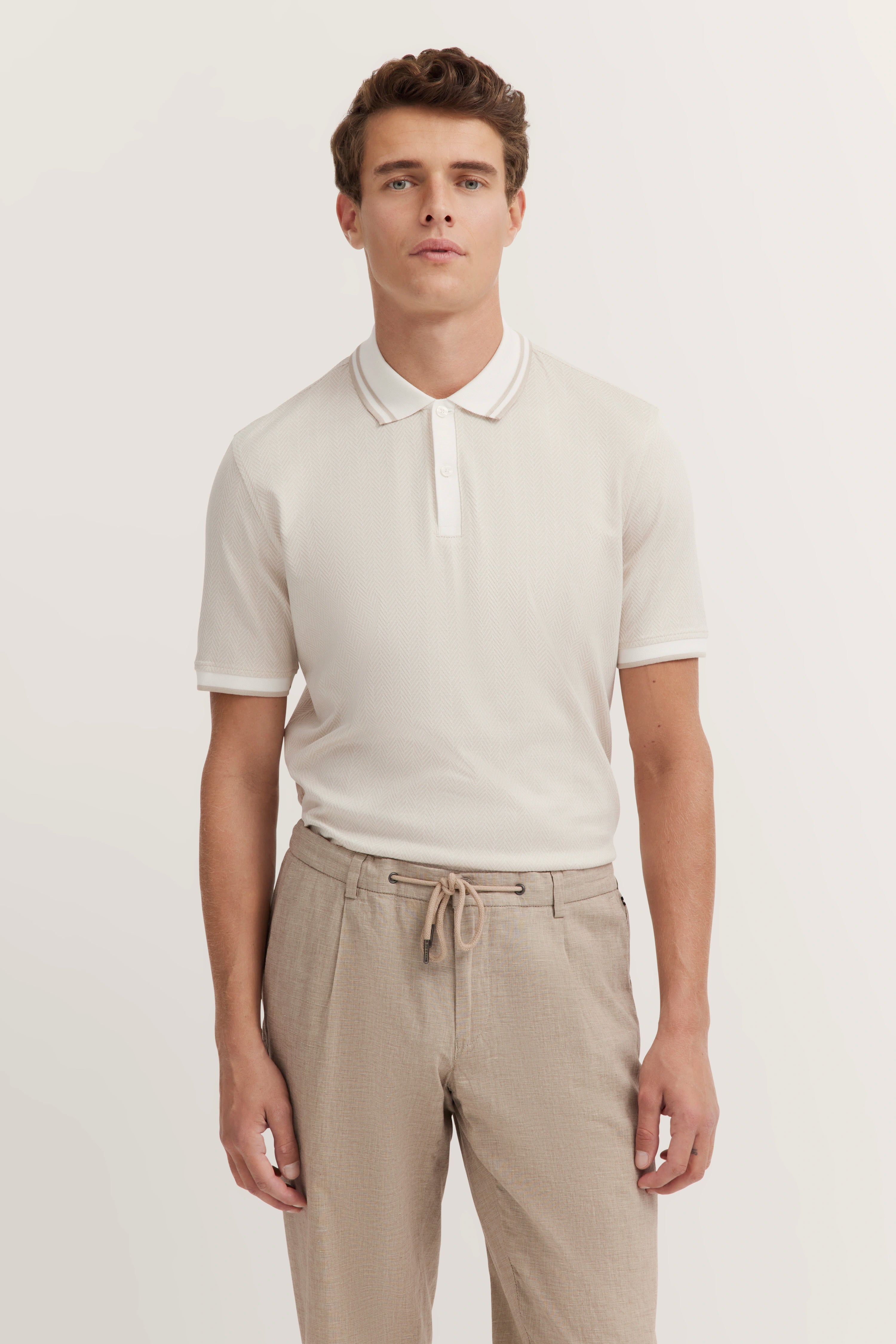 White polo shirt, beige trousers, model standing, relaxed pose, embodying bugatti's timeless elegance and Italian flair.