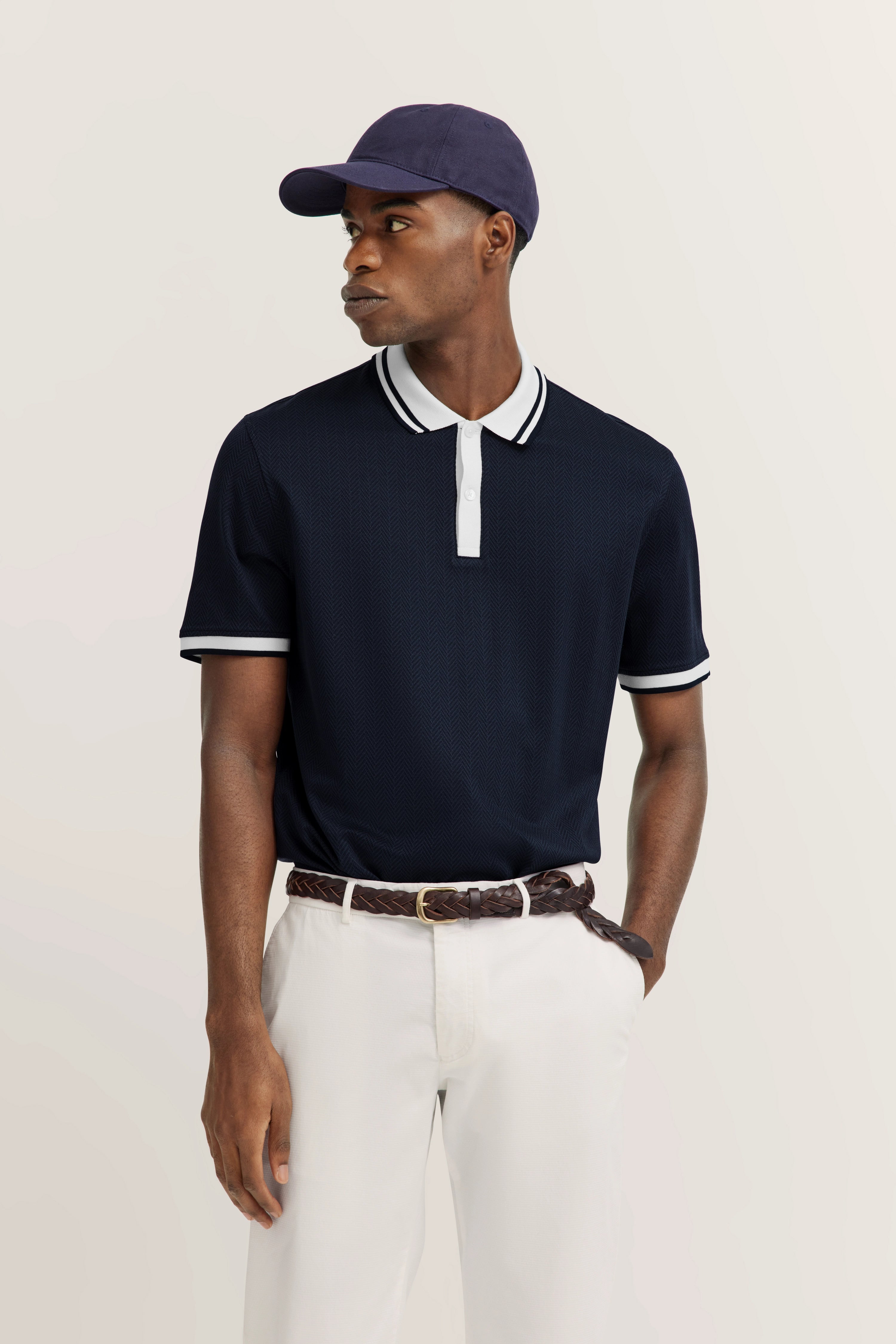 Navy blue polo with white accents, white pants, brown belt, model posing relaxed, bugatti style.