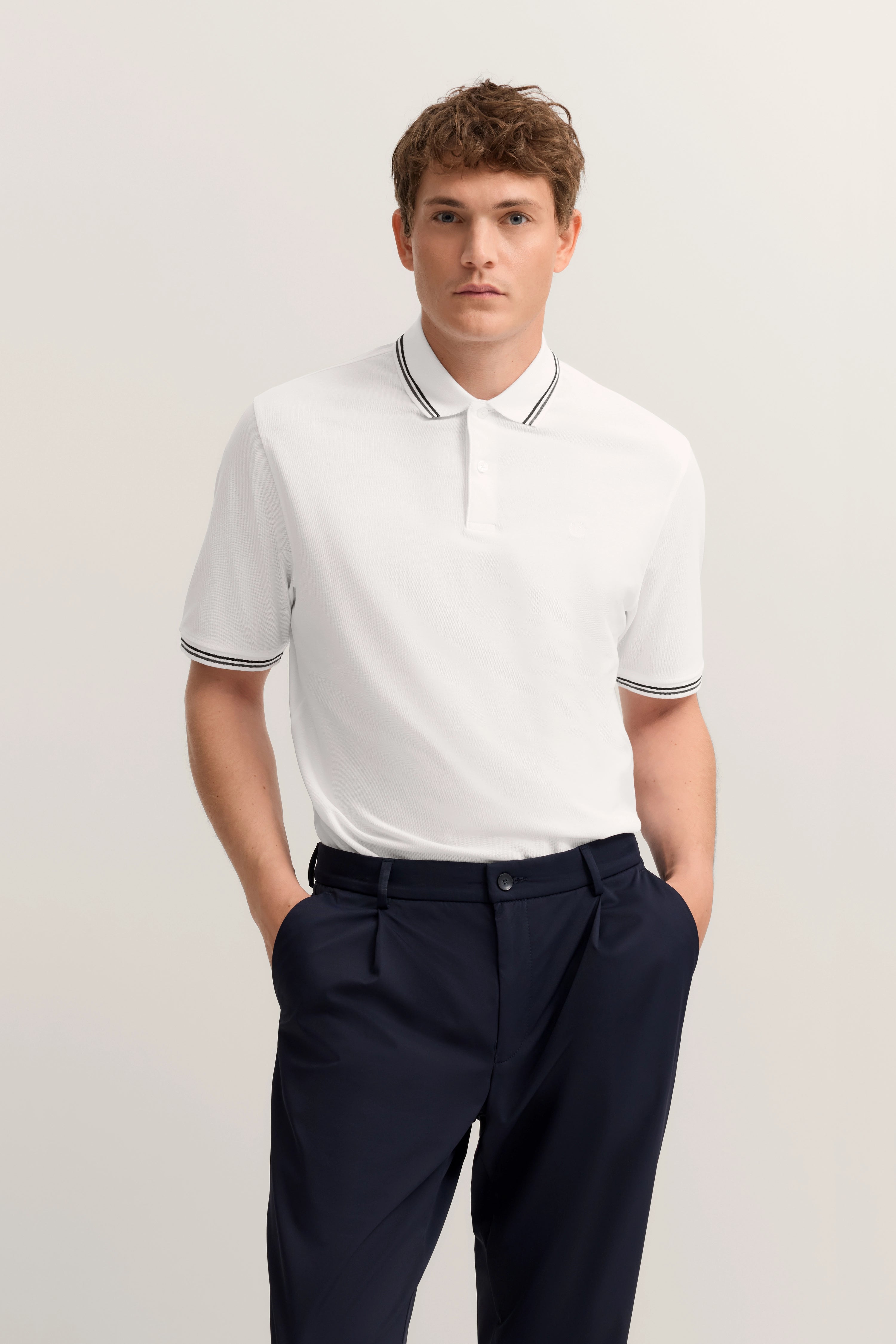 Weiße Polo, blaue Hose, Model mit entspanntem Blick, bugatti Stil.