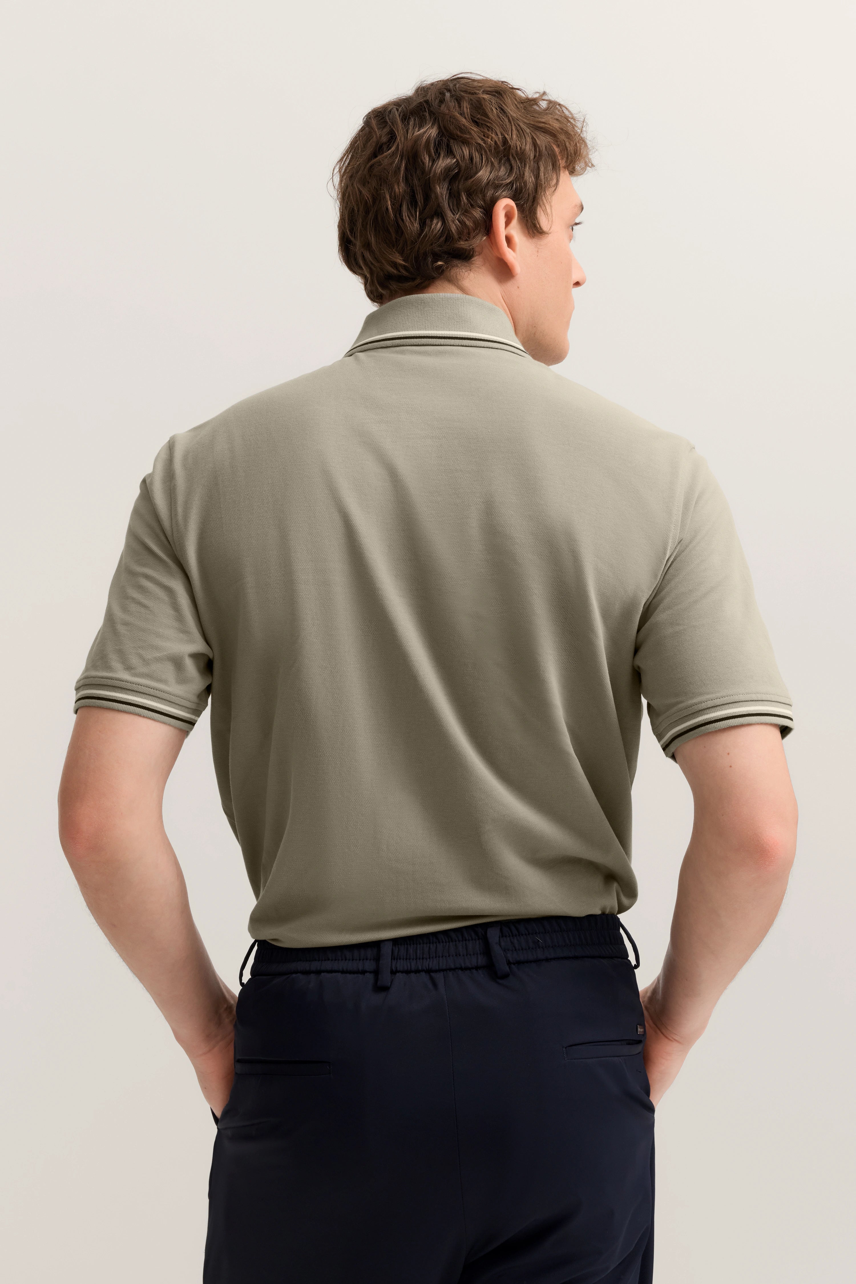 Rückansicht Model in olivgrünem Polo und dunkelblauer Hose von bugatti, leger und stilvoll.