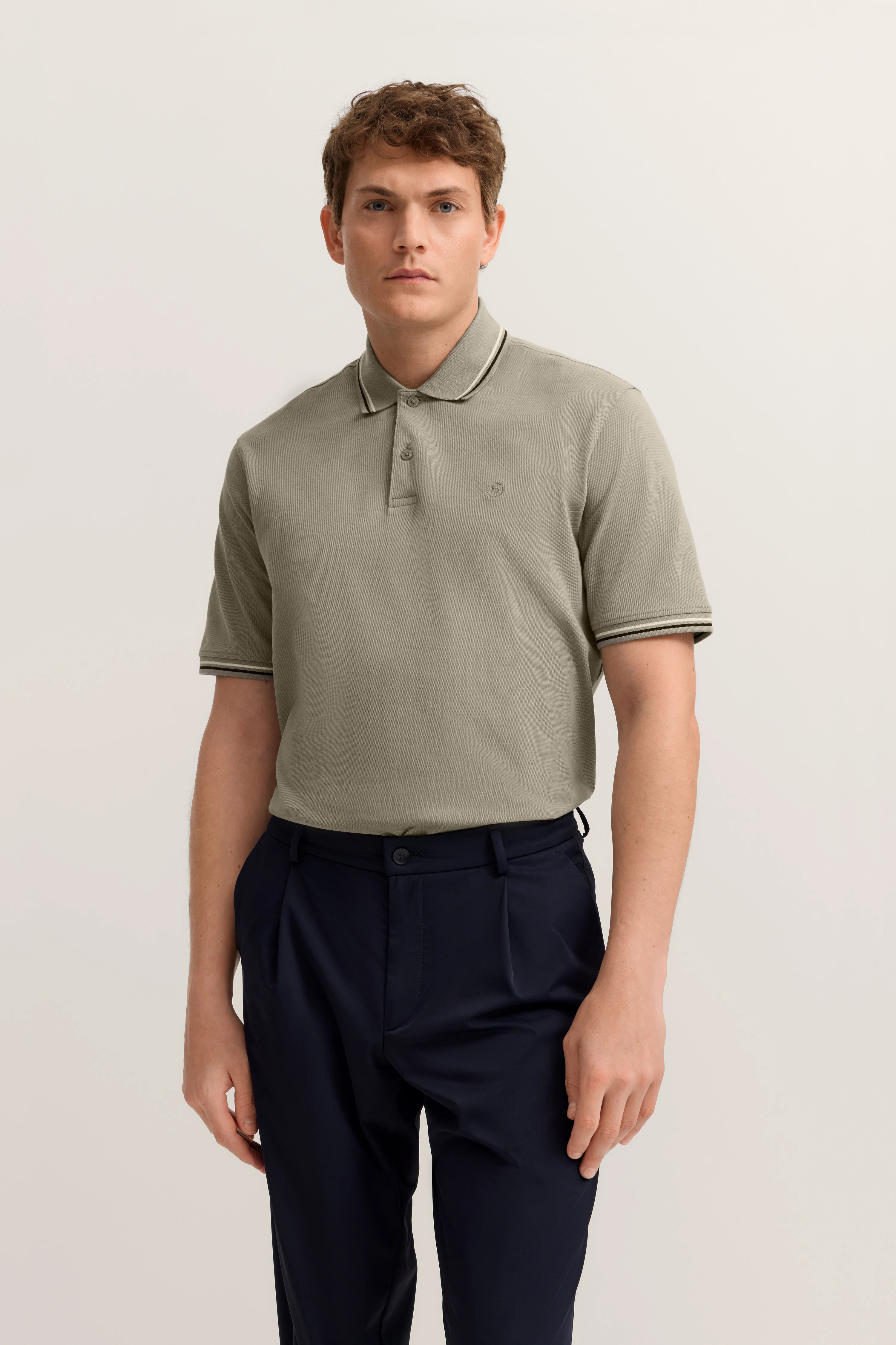 bugatti Model in olivgrünem Polo und dunkelblauer Hose, legeres Posing, entspannter Stil.