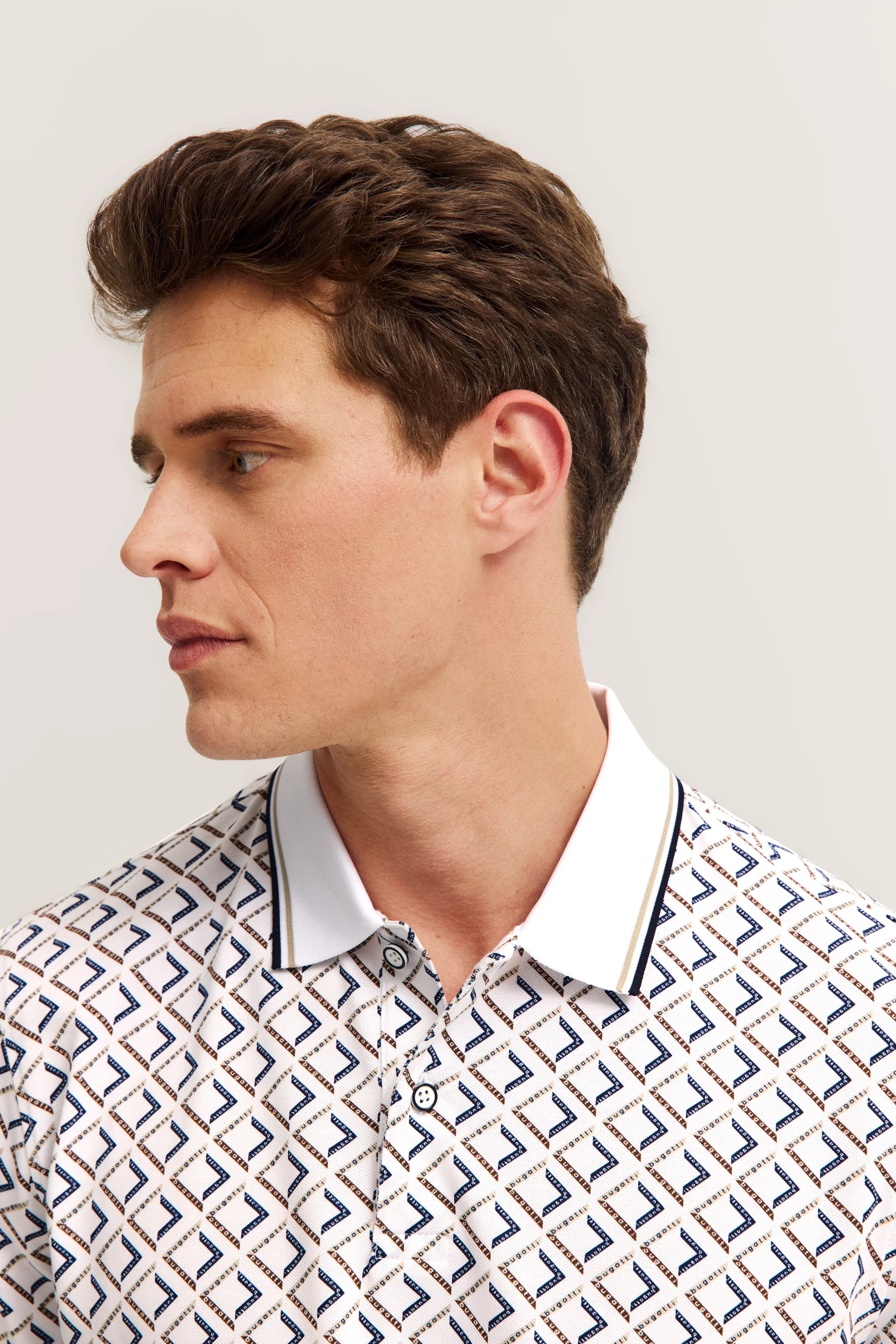 Büstenbild eines Mannes mit weißem bugatti Poloshirt, geometrisches Muster in Blau und Braun.
