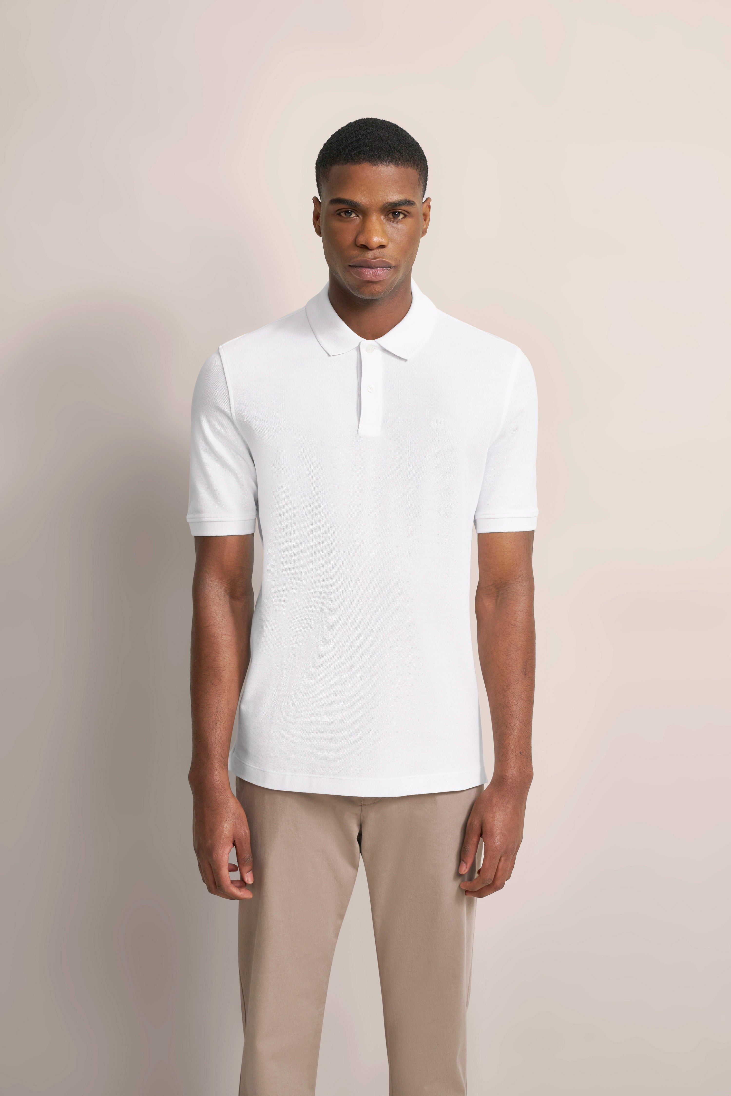 bugatti model in white polo shirt and beige chinos, standing stylishly and casually.