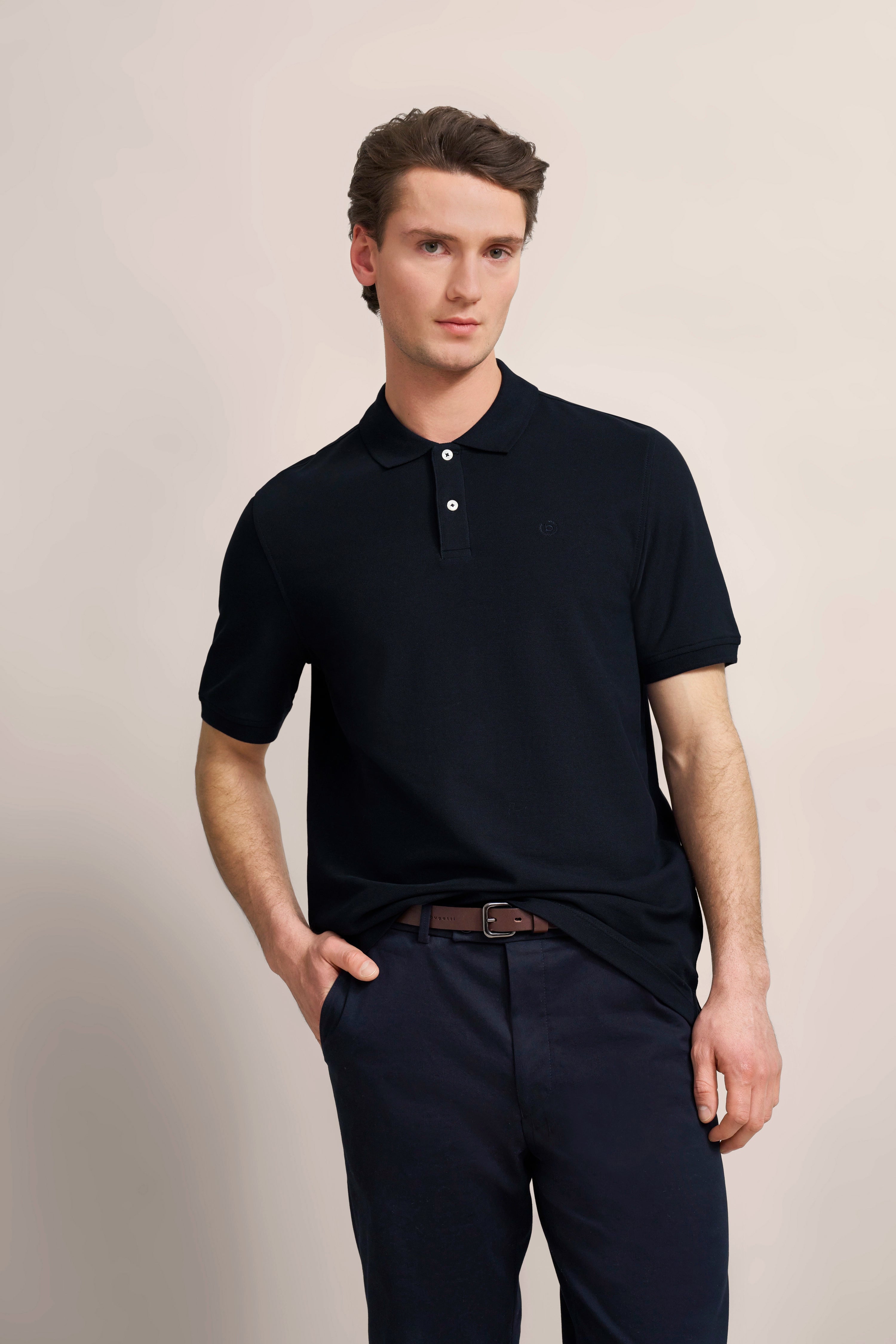 bugatti model: Black polo shirt, blue pants, relaxed pose with hands in pockets.