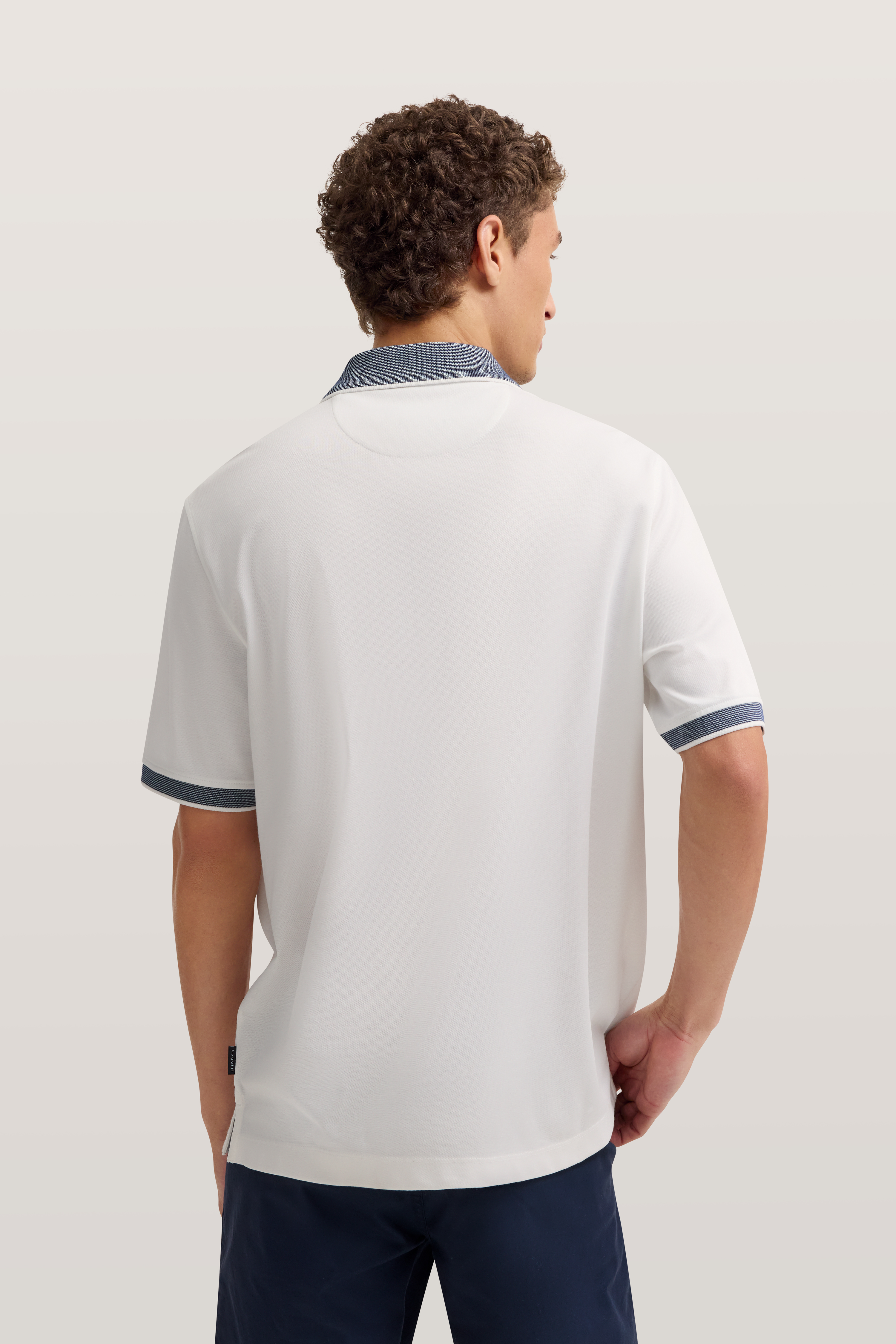 Weißes Polohemd mit blauem Kragen, Rückansicht, getragen von Model in entspannter Pose.
