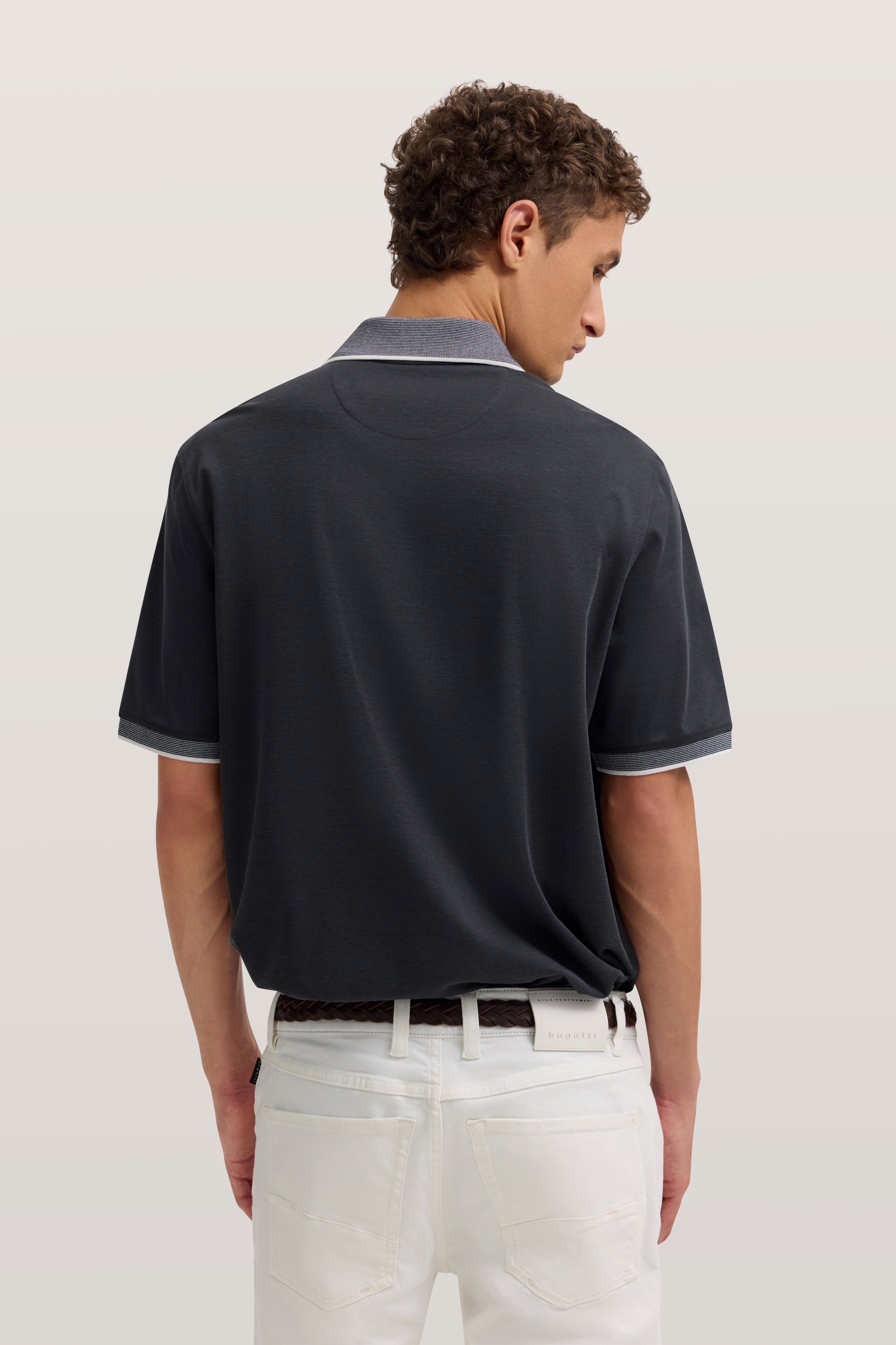 Dunkelblaues Polohemd und weiße Jeans, Rückansicht Model, lässig posierend.
