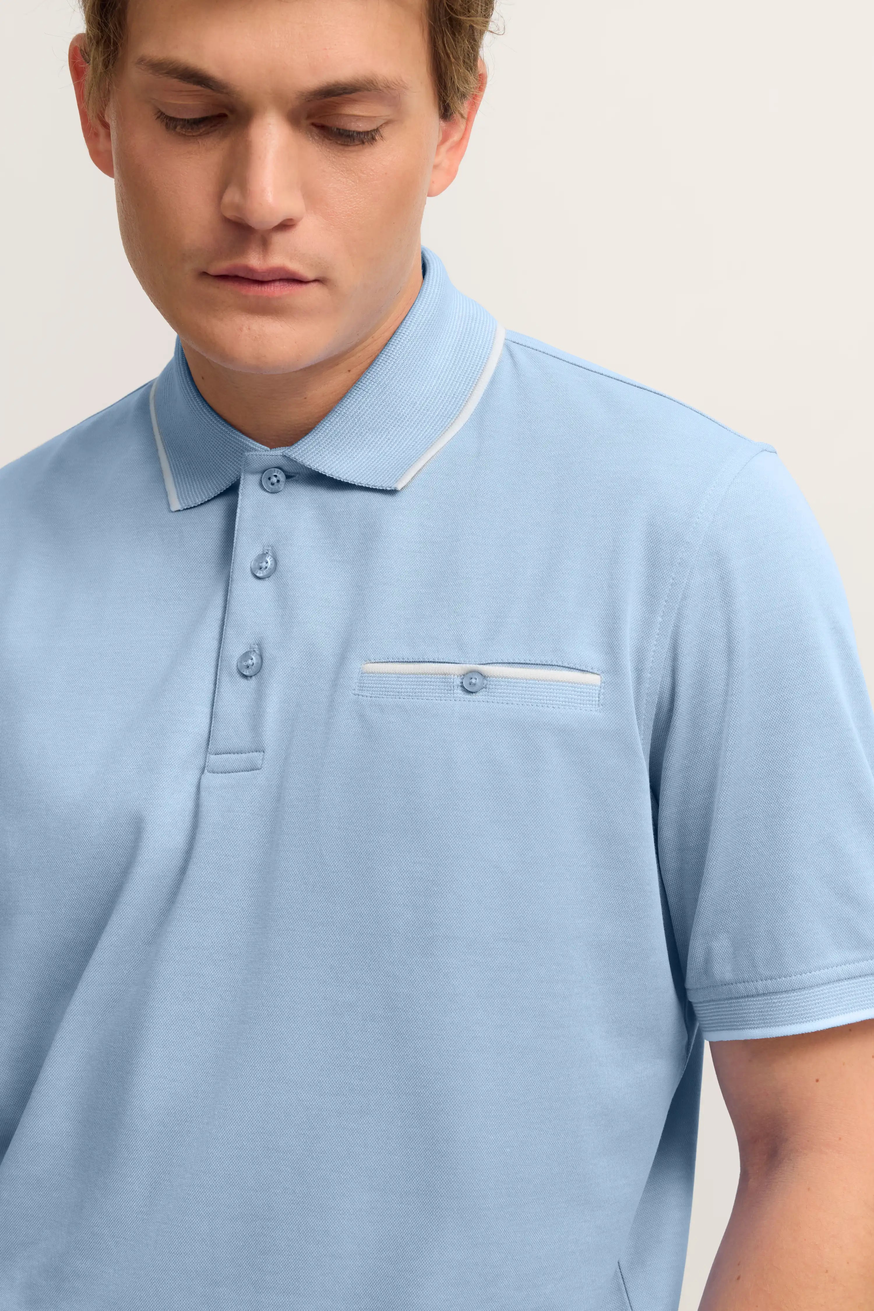 Hellblaues Polohemd mit Knopfleiste und Brusttasche, Modelbild, entspannte Pose.