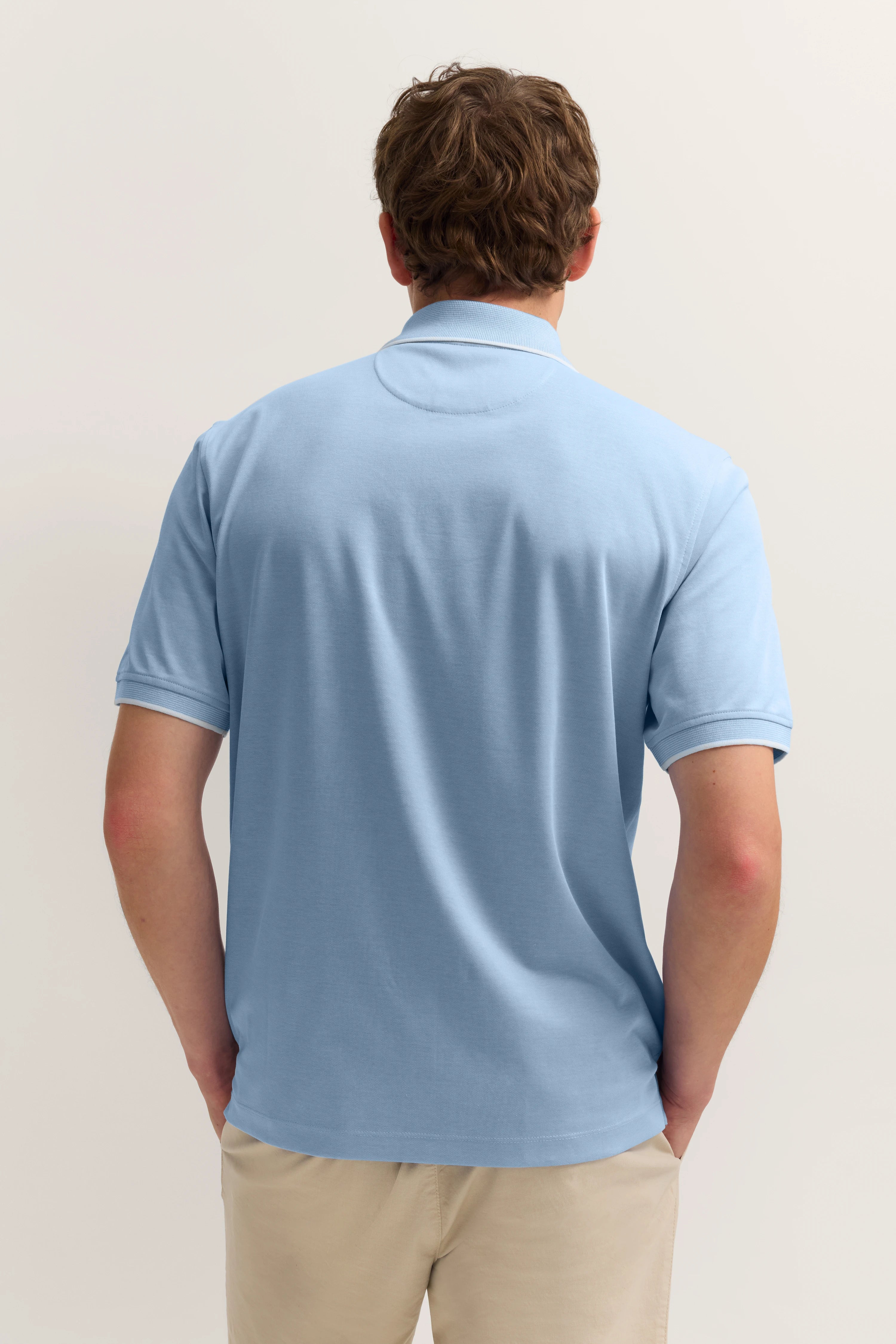Hellblaues Polohemd, Rückansicht, legeres Modelbild, entspannte Haltung.