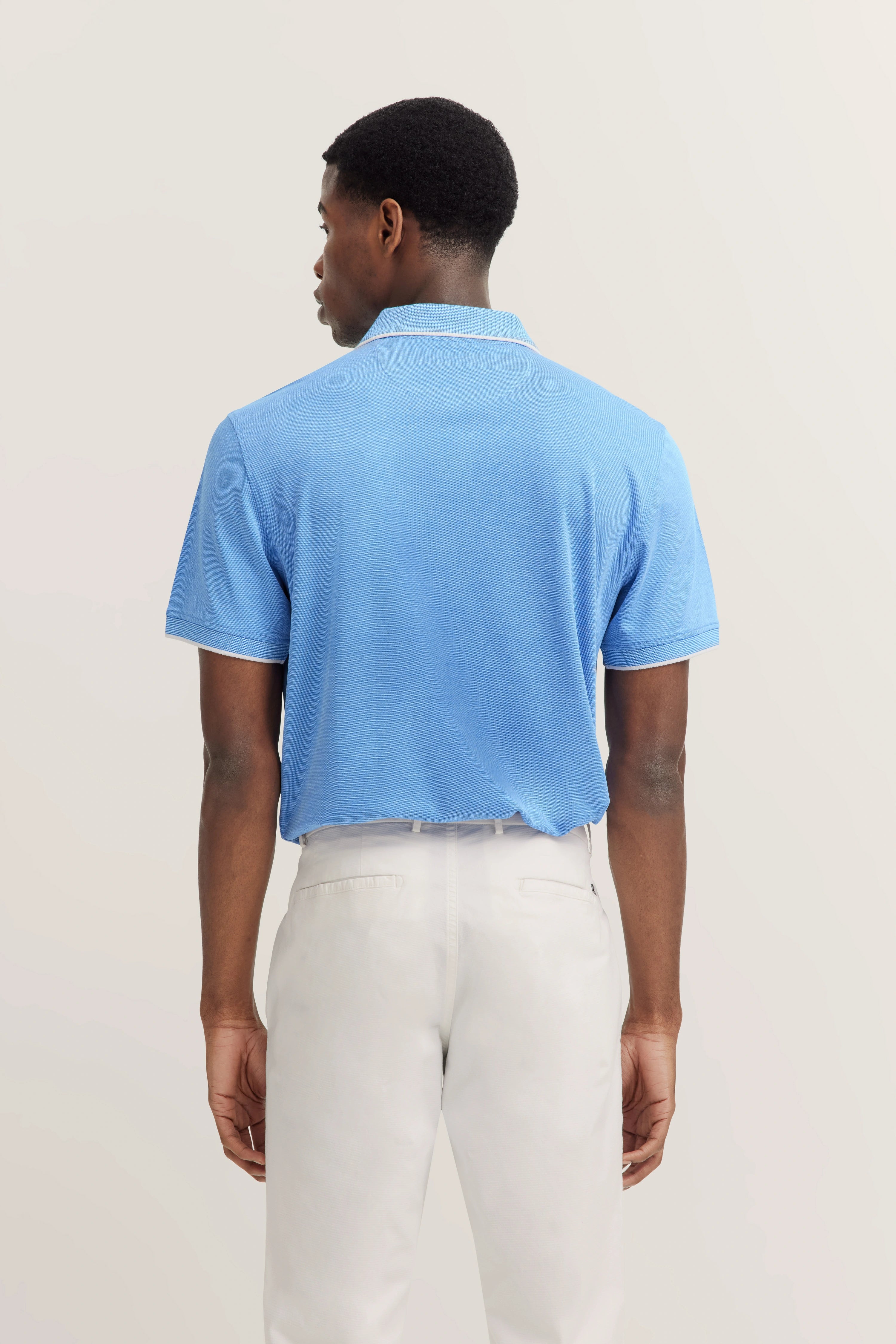 Model in blue bugatti polo and white pants from behind.