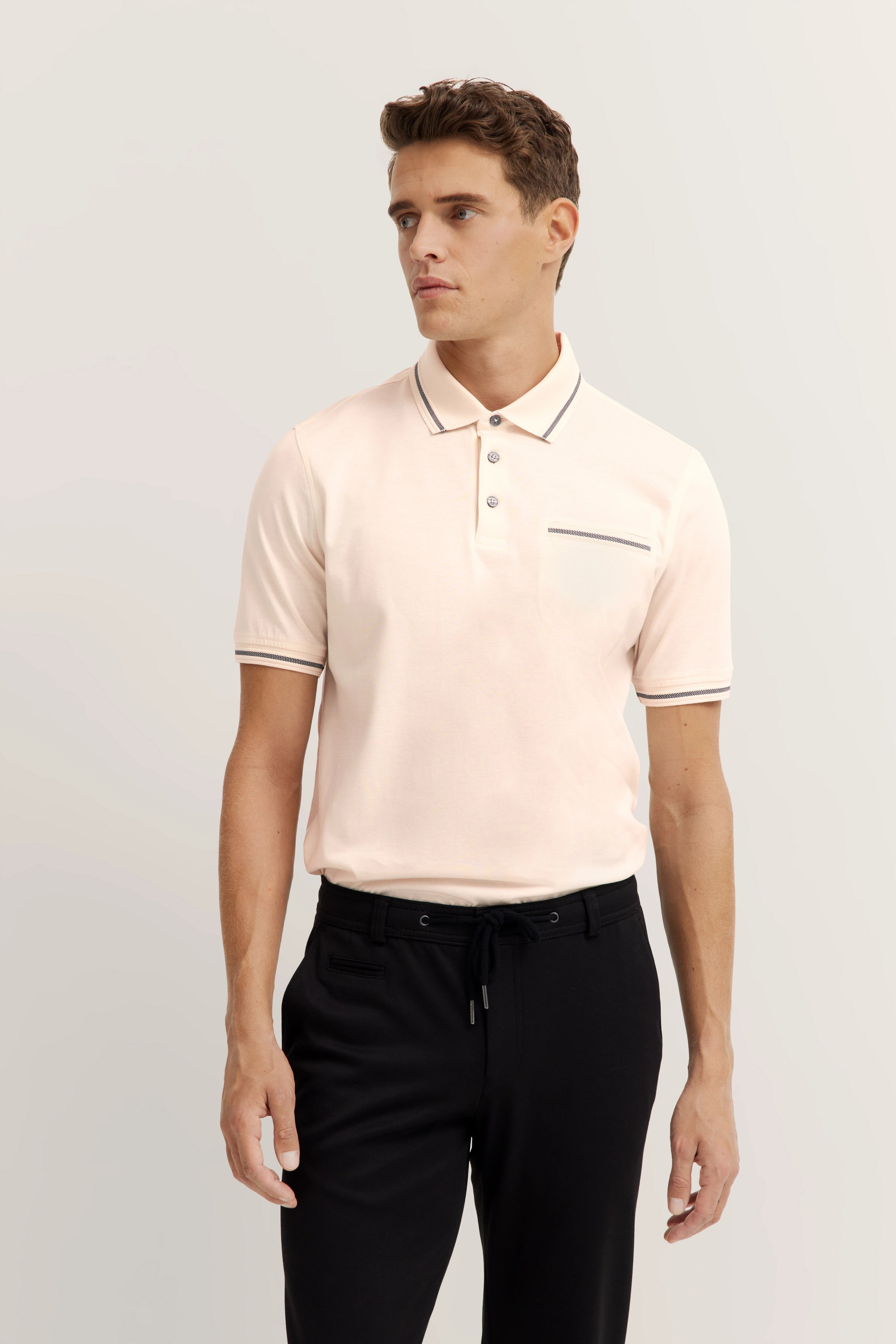 Male model in light bugatti polo and black pants, relaxed pose.