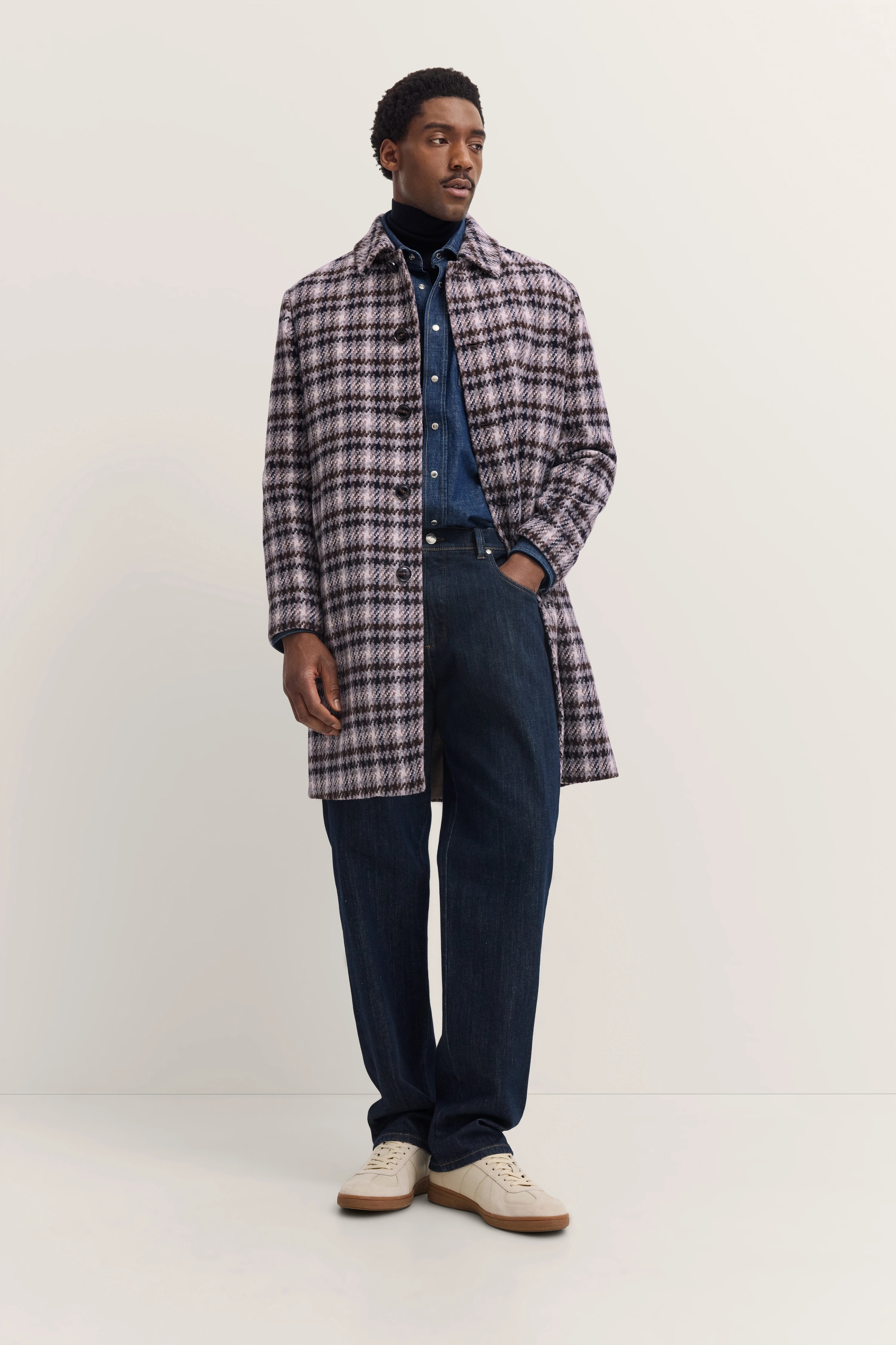 Model draagt geruite bugatti-jas, blauw jeanspak en witte sneakers, casual pose.