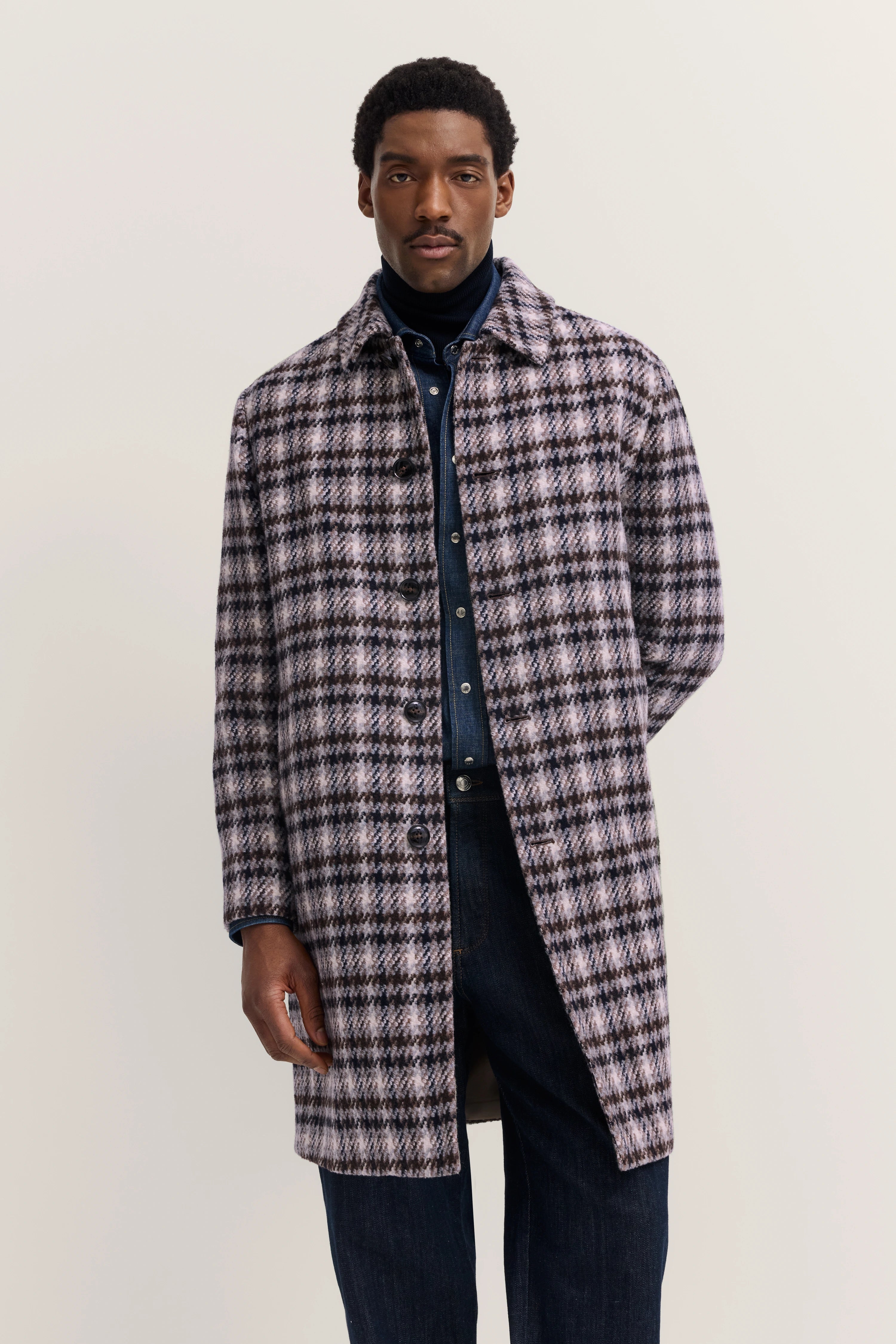 Model mit kariertem bugatti-Mantel in Grau und Blau, dunkles Denim-Outfit, entspannte Pose.