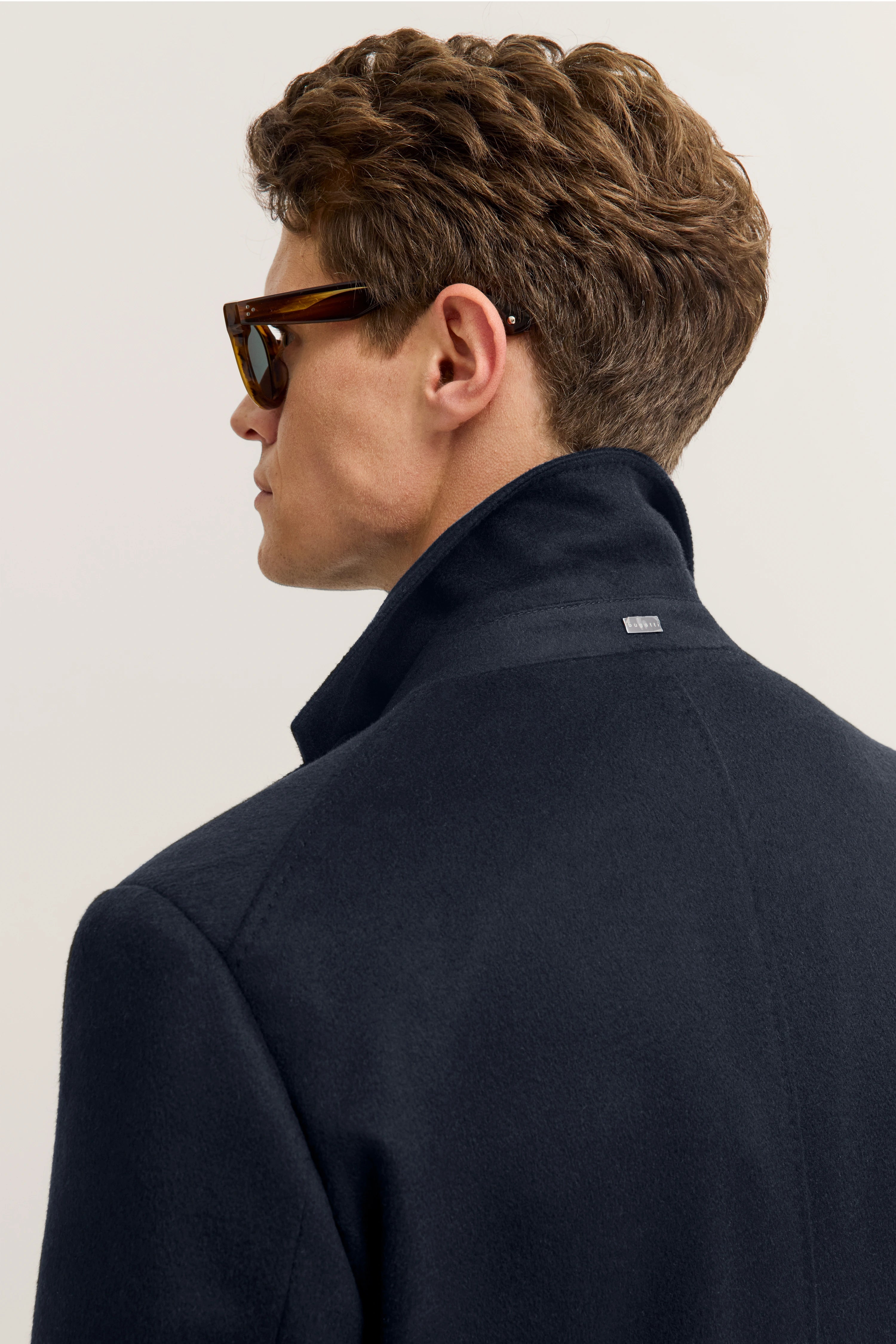 Model in dunkelblauem bugatti Mantel, seitlich, mit hochgestelltem Kragen und Sonnenbrille.