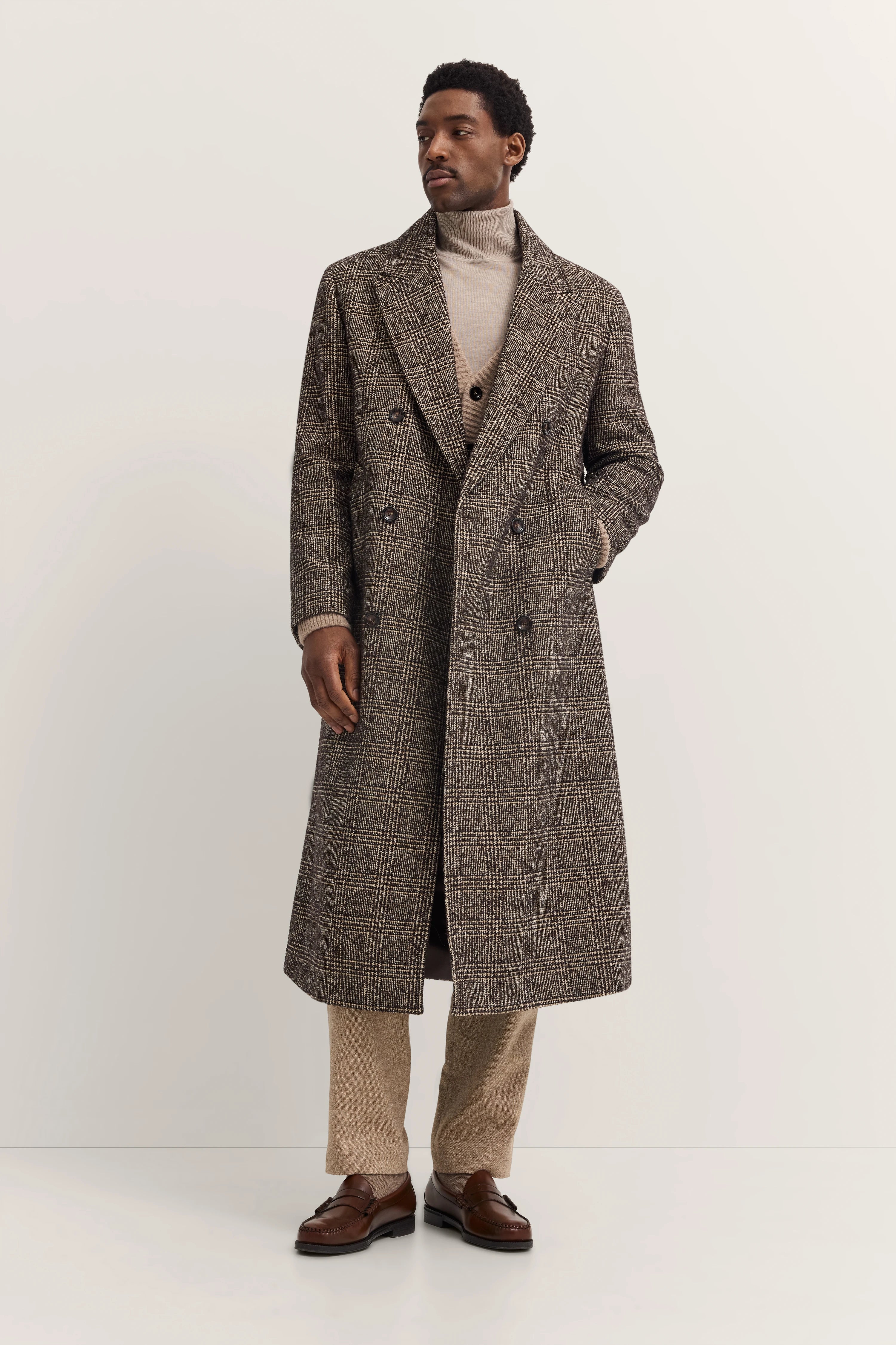 Herrenmodell in kariertem bugatti-Mantel, beiger Rollkragen, braune Schuhe, lässige Pose.