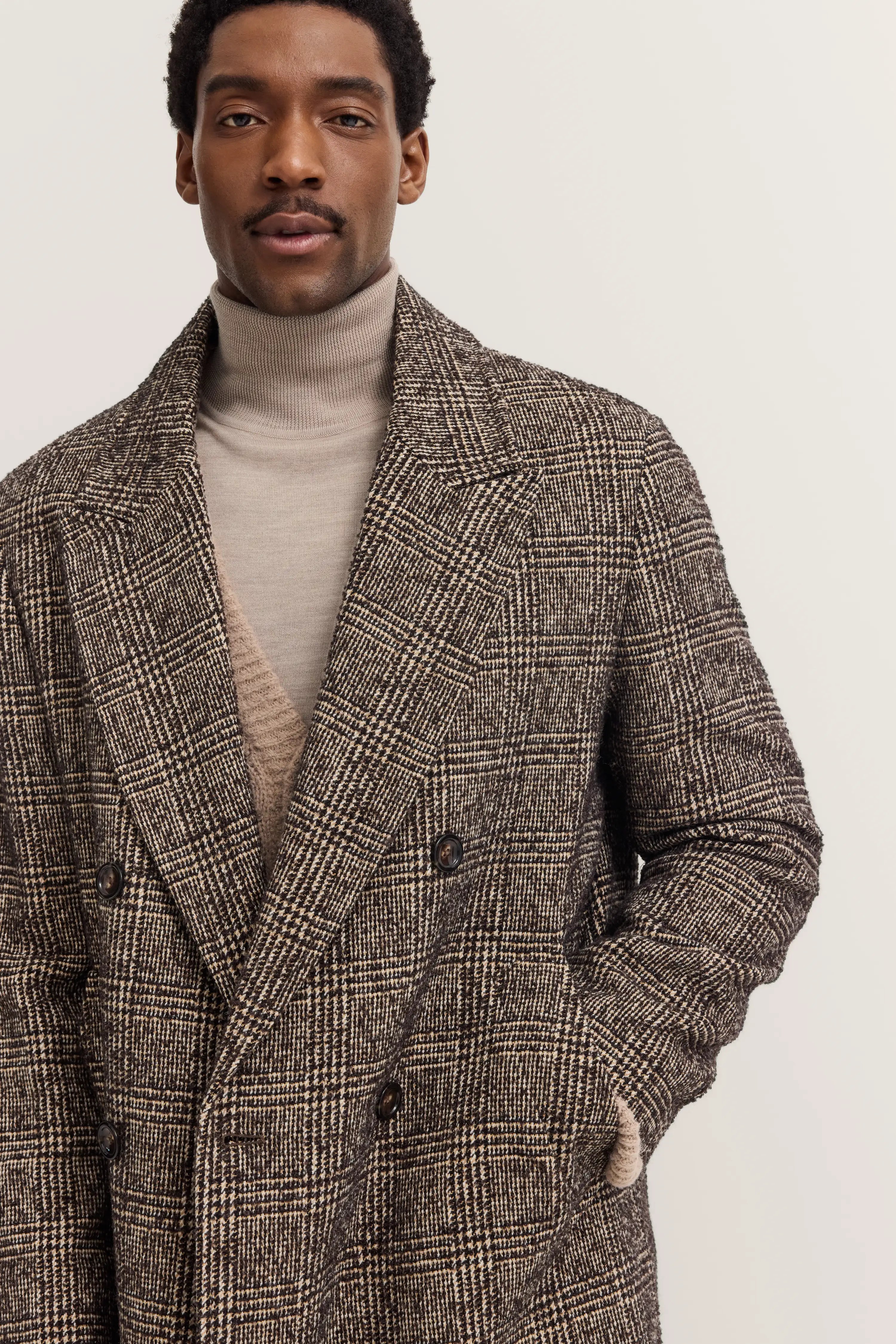 Model trägt karierten Mantel mit Rollkragenpullover in Beige, legeres Posing.