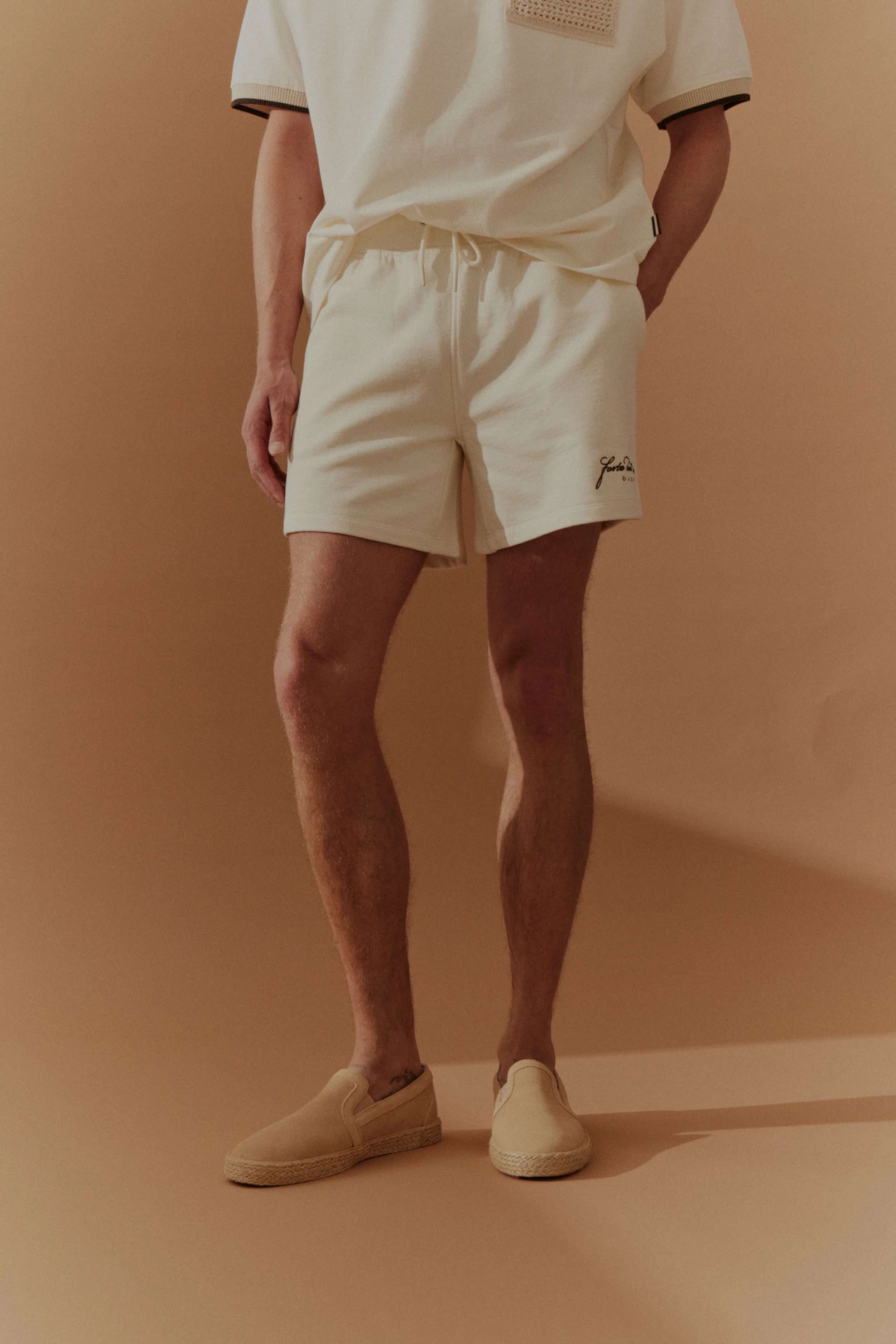 Herren-Shorts in Creme mit passendem T-Shirt, legeres Modelbild, entspannte Pose.