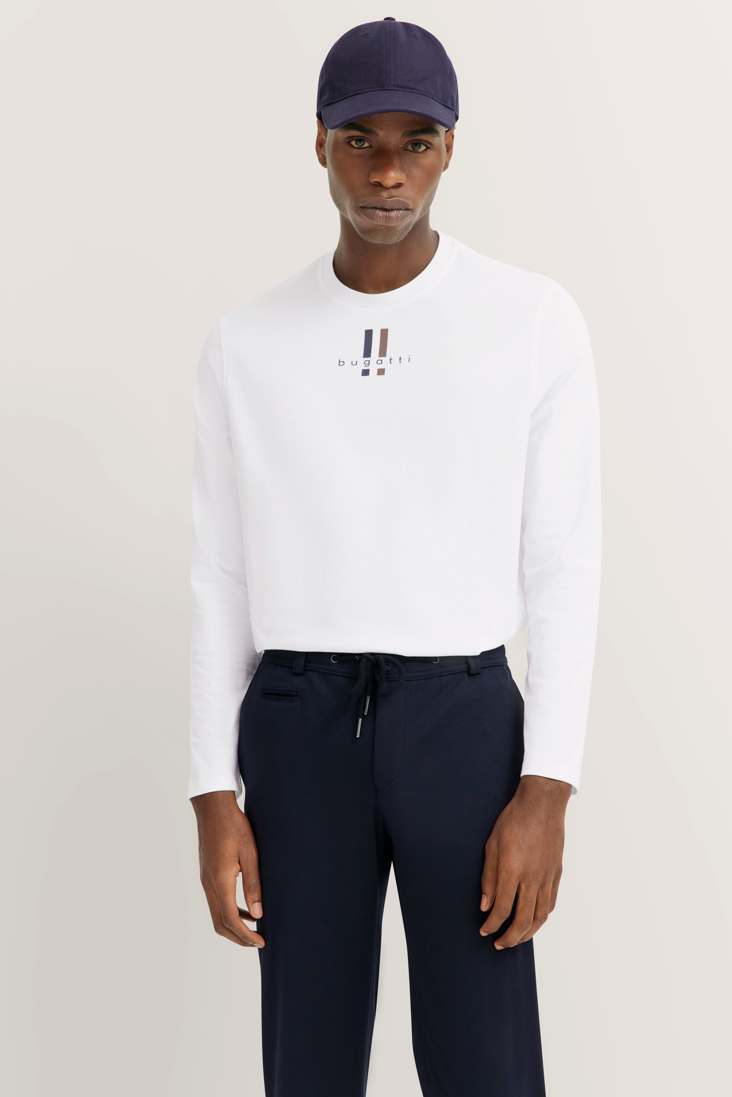 White bugatti long-sleeve shirt, navy pants, model facing forward with baseball cap.