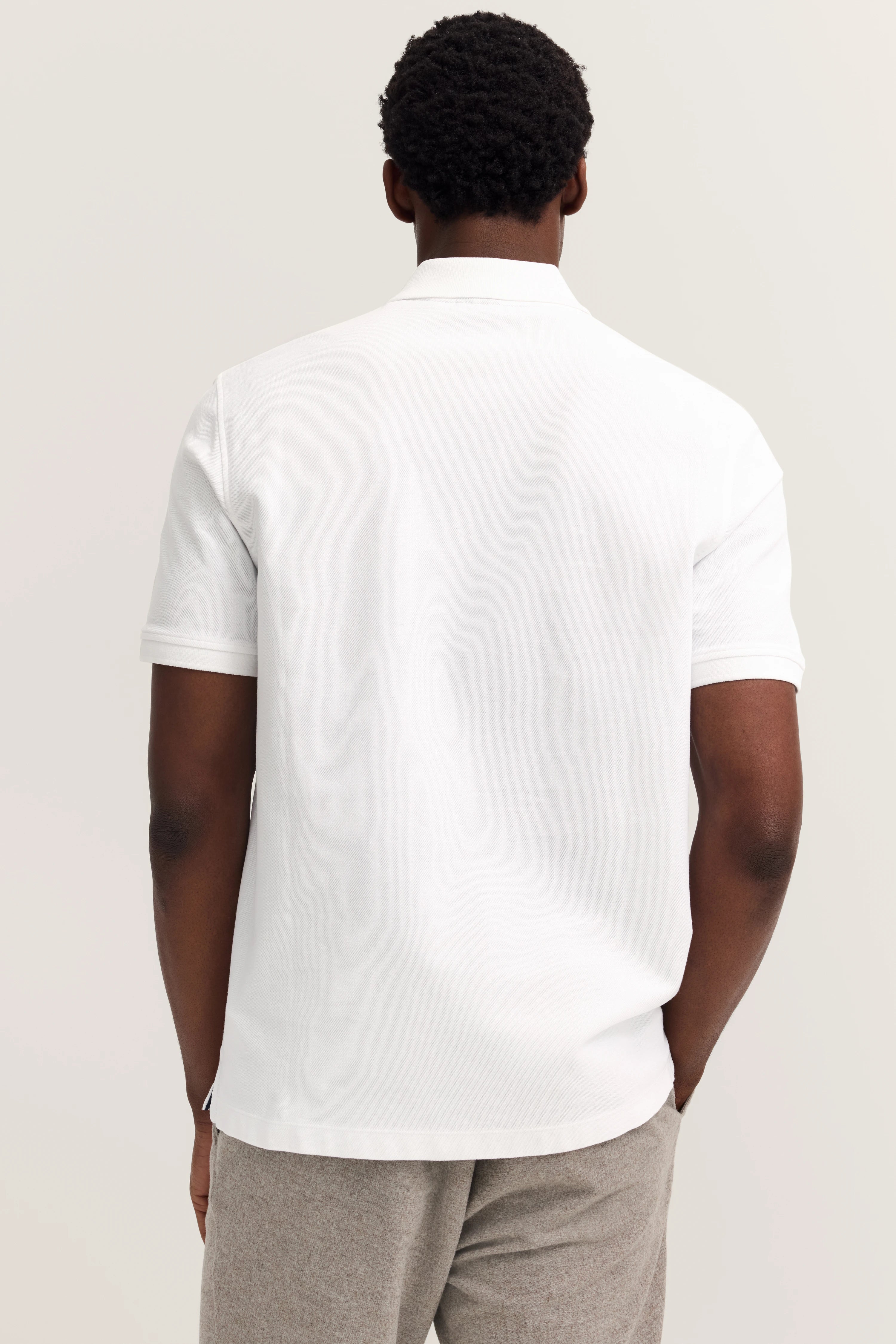 White bugatti polo shirt, back view, casually worn, paired with gray pants.