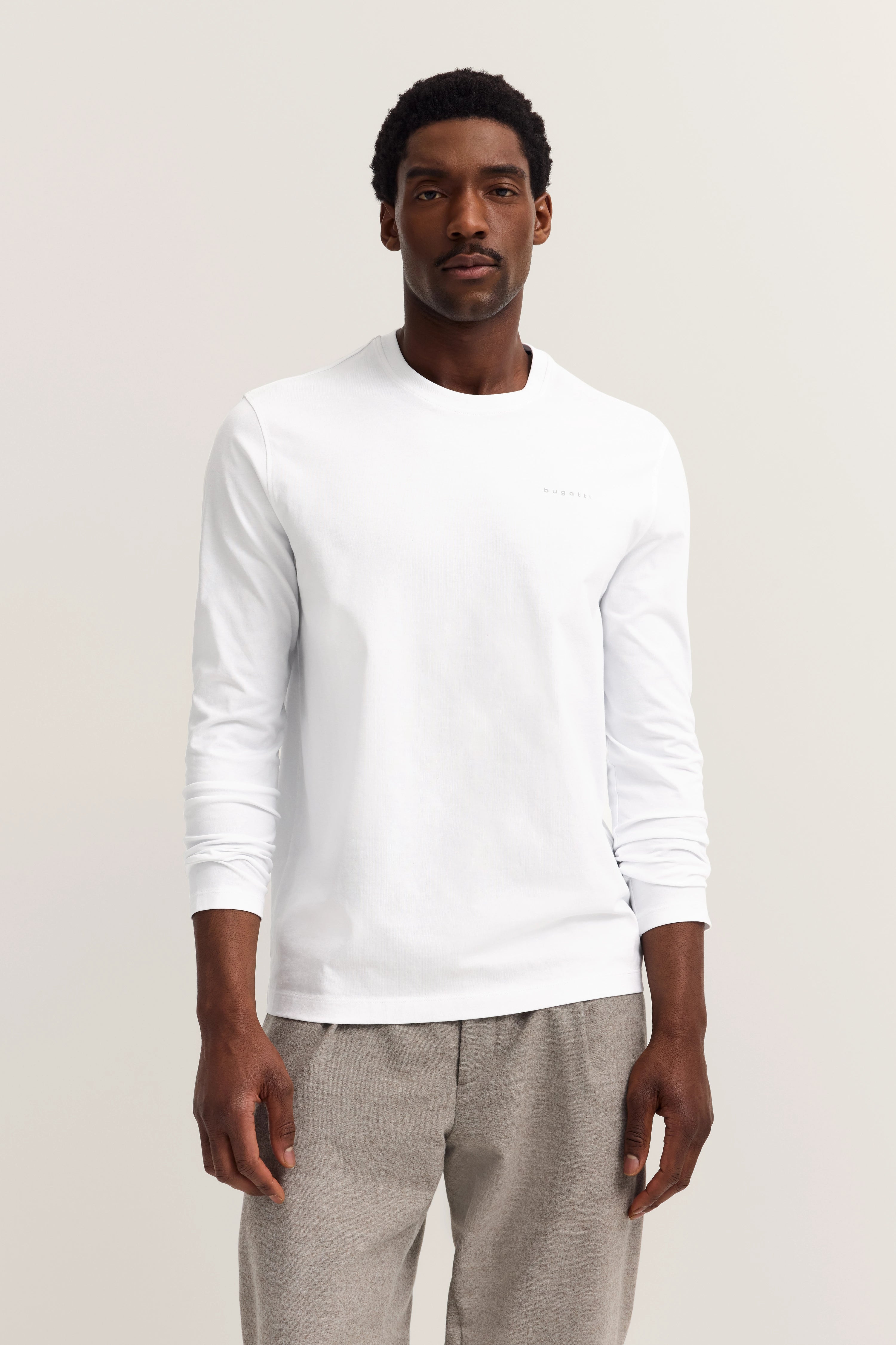 White bugatti long-sleeve shirt with gray pants, model in relaxed pose.