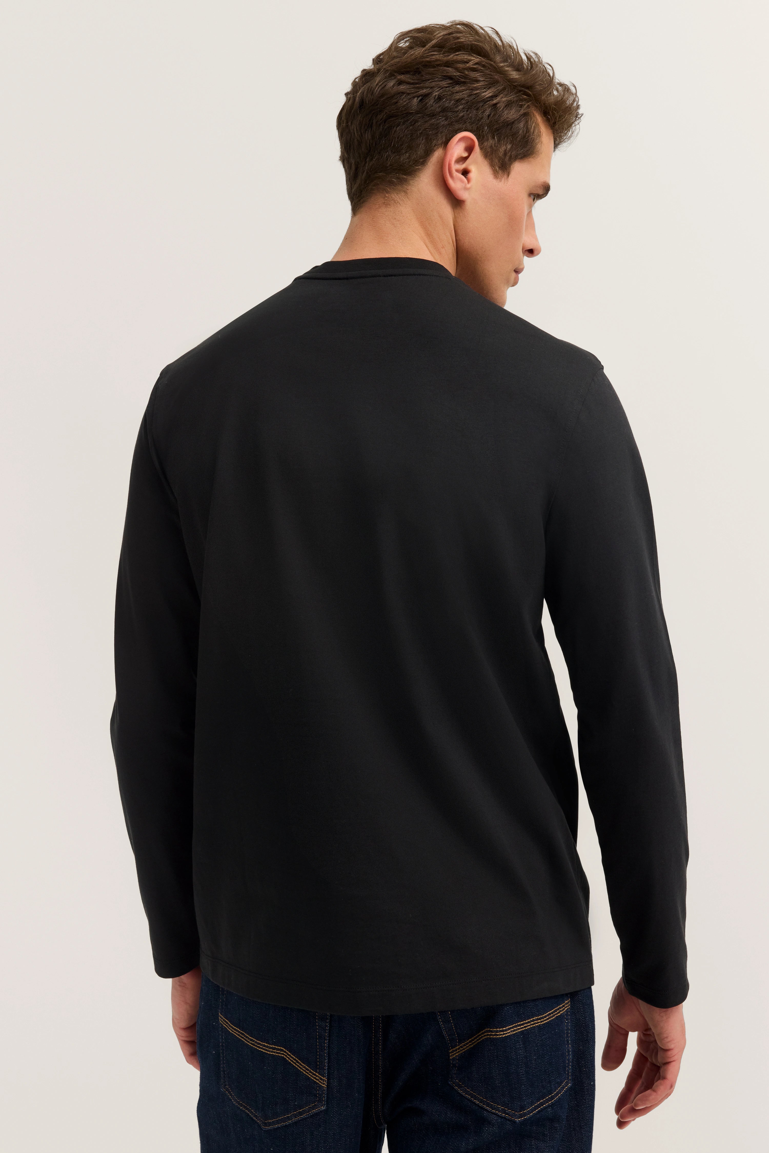 bugatti model: Zwart lang shirt, jeans, achterkant, ontspannen pose.