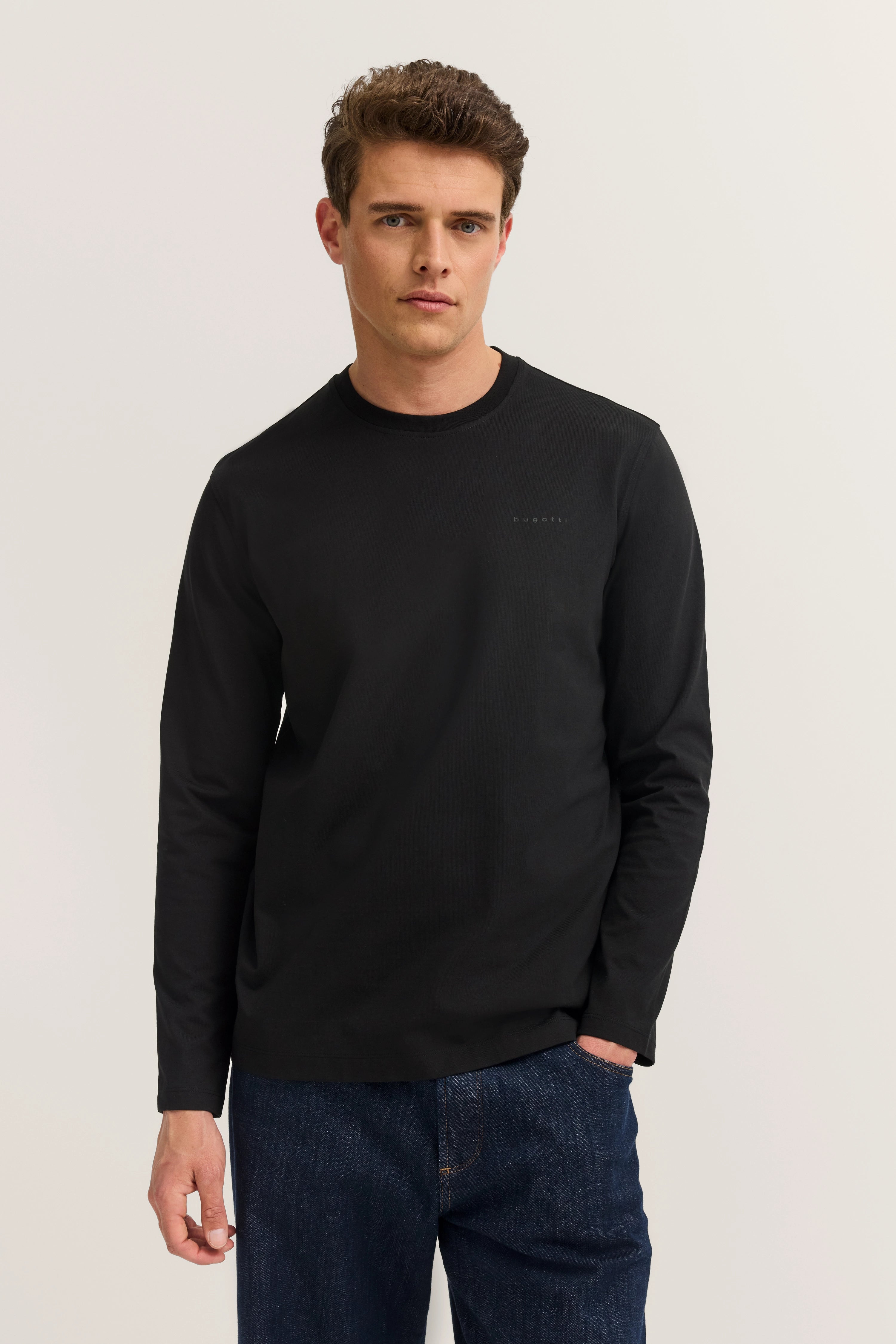 Model wearing black bugatti long-sleeve shirt and blue jeans, casual pose, classic and stylish.