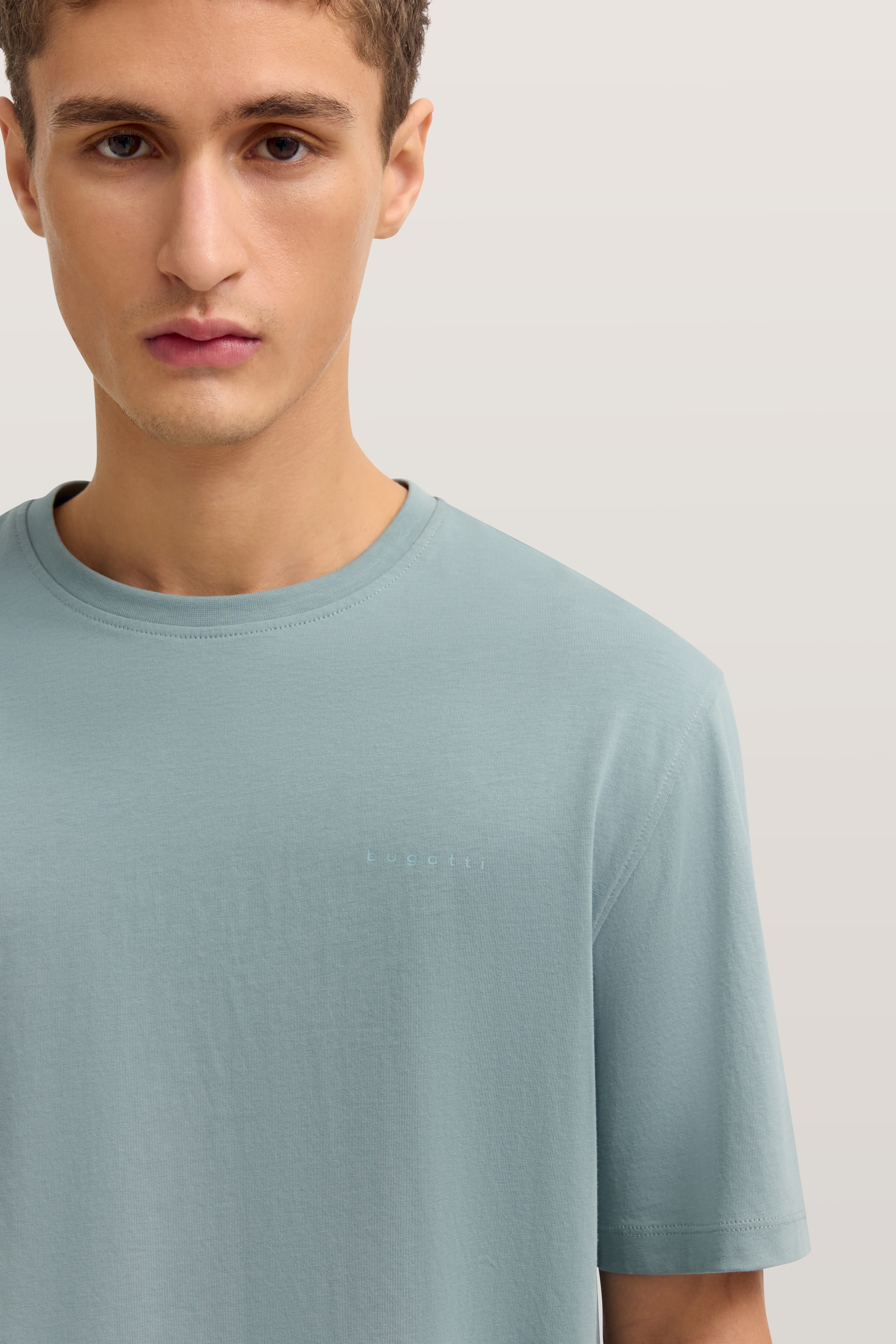 bugatti Modelbild, hellblaues T-Shirt, legeres Posing, minimalistisches Design.