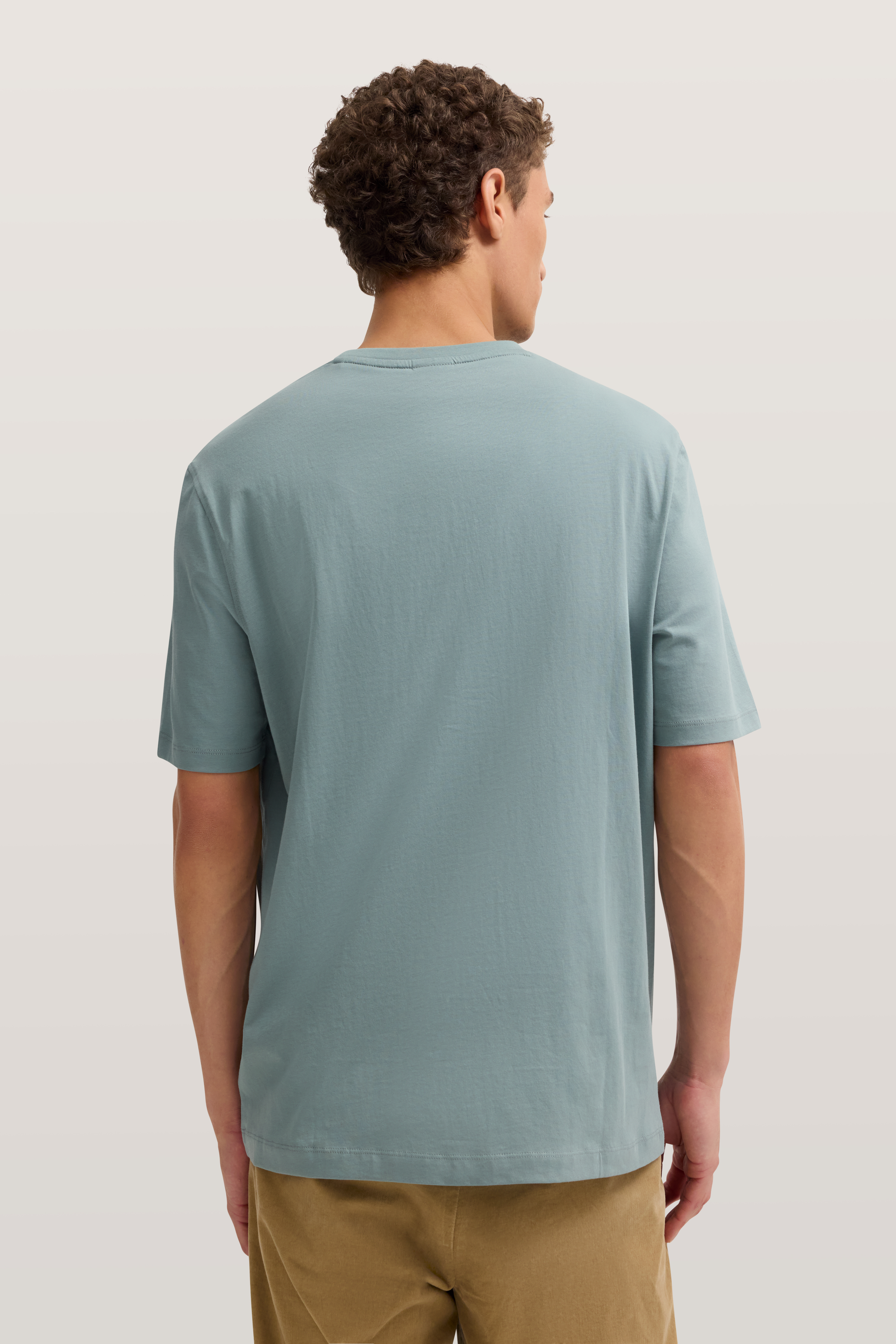 Rückansicht eines Models im legeren Outfit mit hellblauem bugatti T-Shirt und beige Hose.