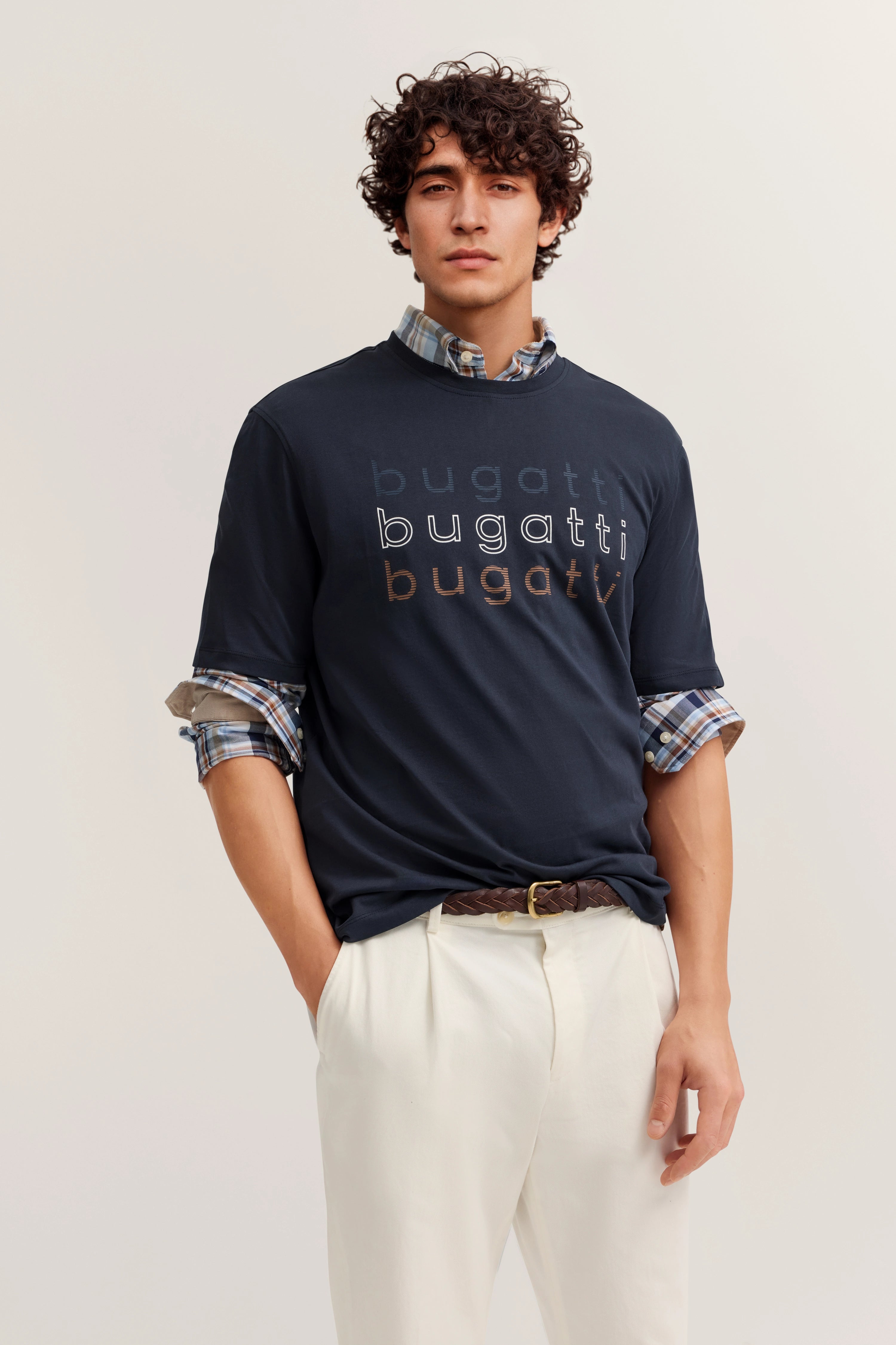 Model im bugatti-Shirt mit Logo, karierte Hemdärmel, leger posierend, weiße Hose.