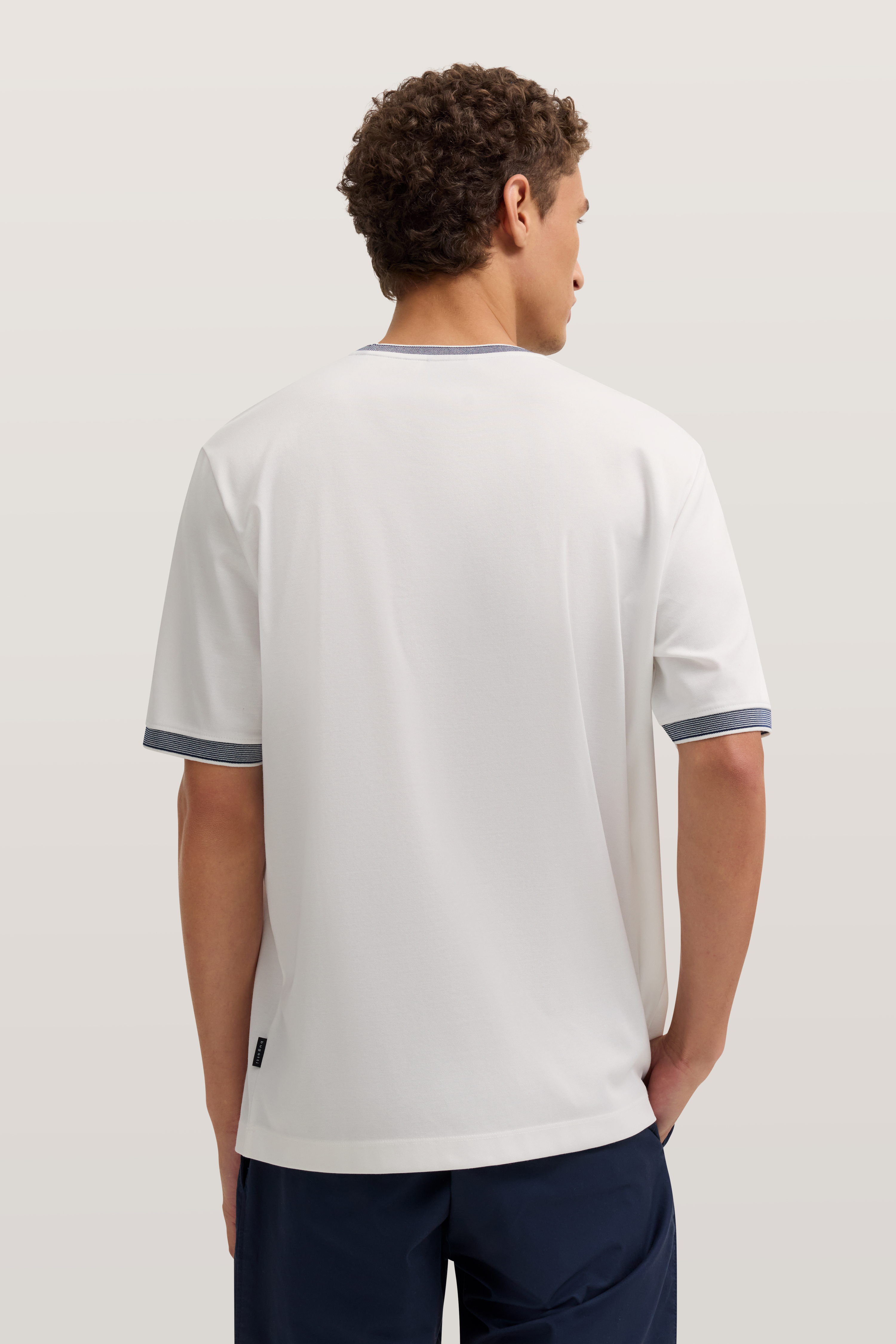 Weißes T-Shirt mit blauen Akzenten, Modelbild von hinten, entspannte Haltung.