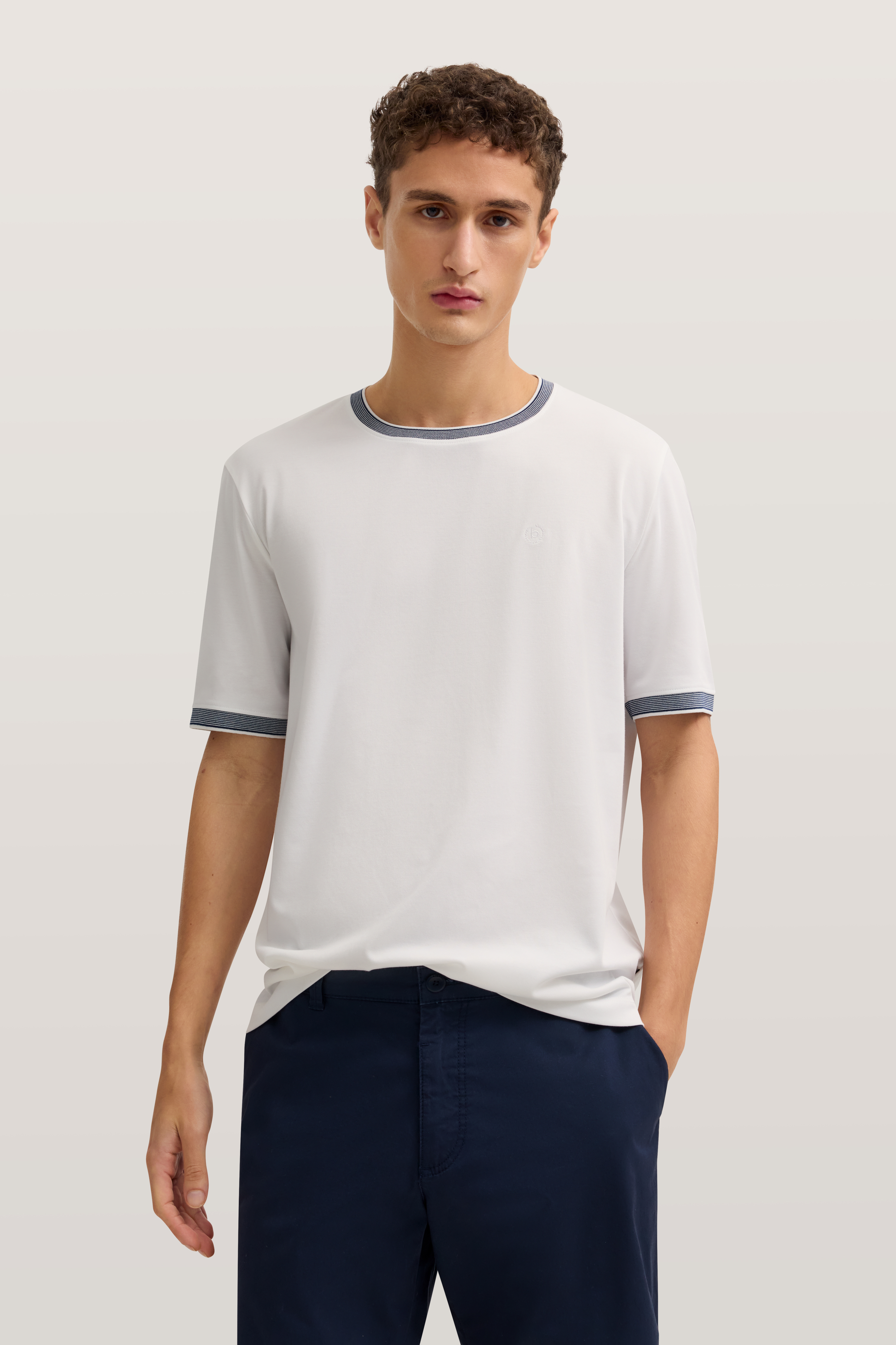 "bugatti Modelbild: weißes T-Shirt mit blauen Details, dunkelblaue Hose, lässiges Posing, entspannt und stilvoll."