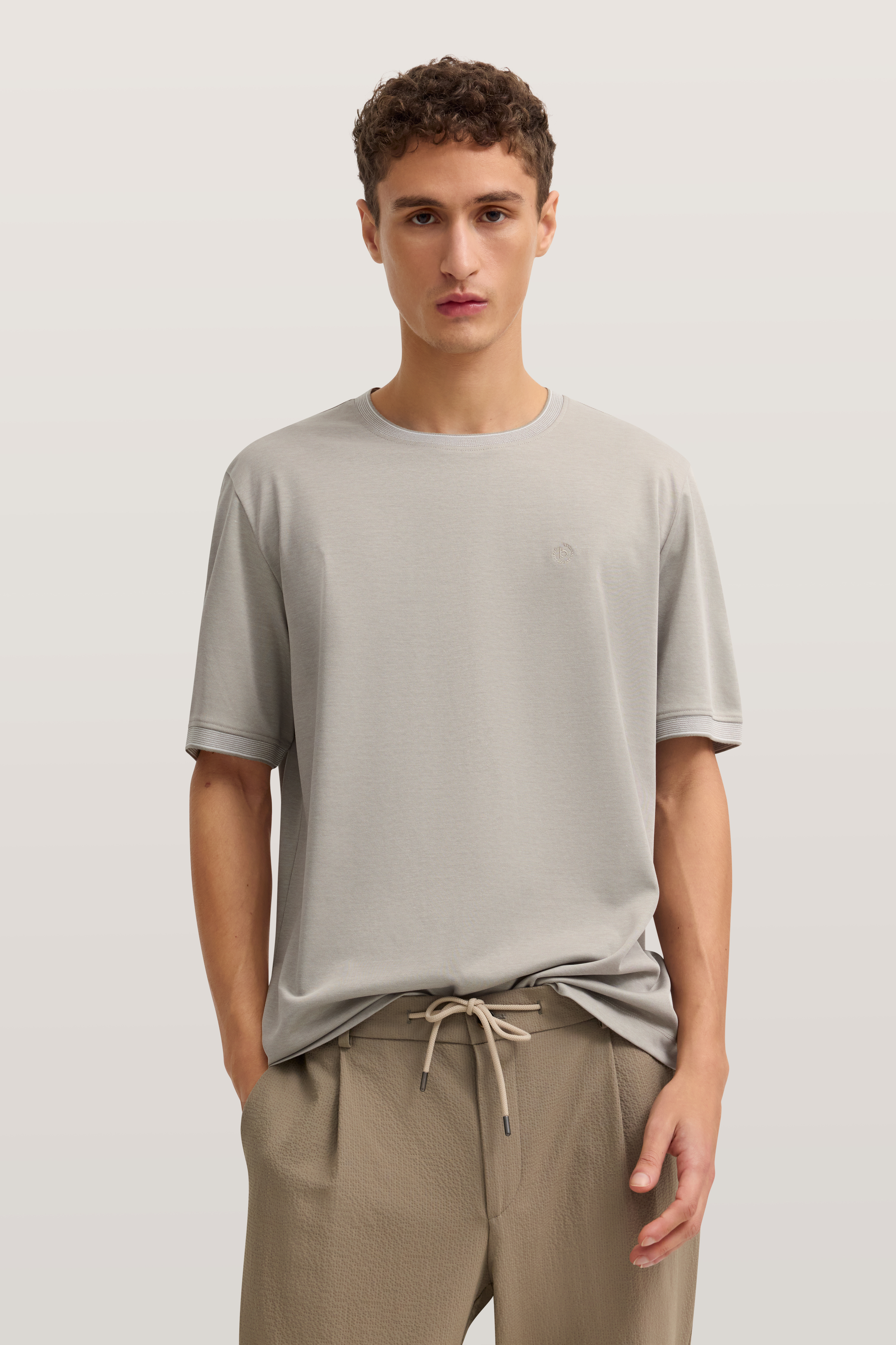 Modelbild mit lässigem, grauem bugatti T-Shirt und beigen Hosen, entspannte Haltung.