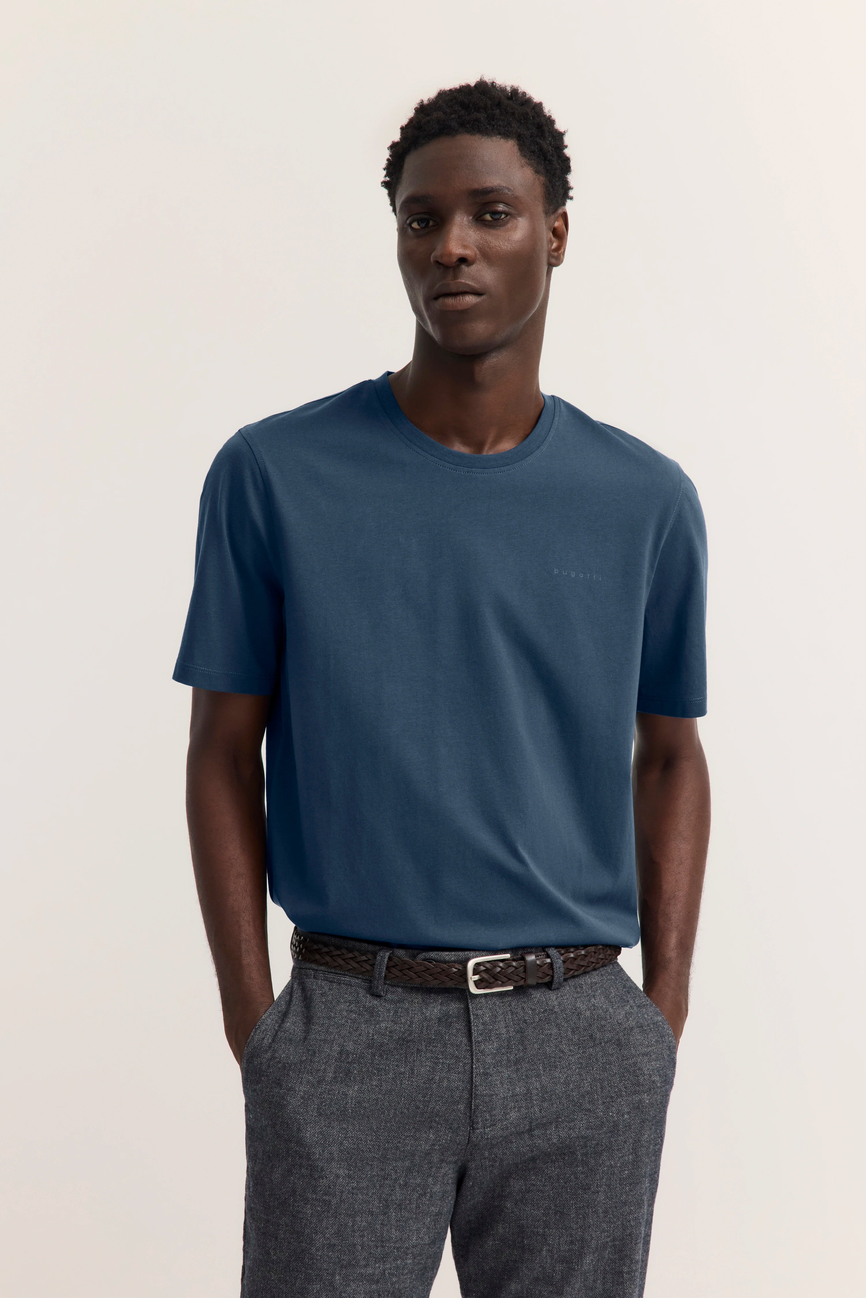 Blaues T-Shirt und graue Hose, Modelbild mit lässiger Pose, bugatti Stil und Eleganz.
