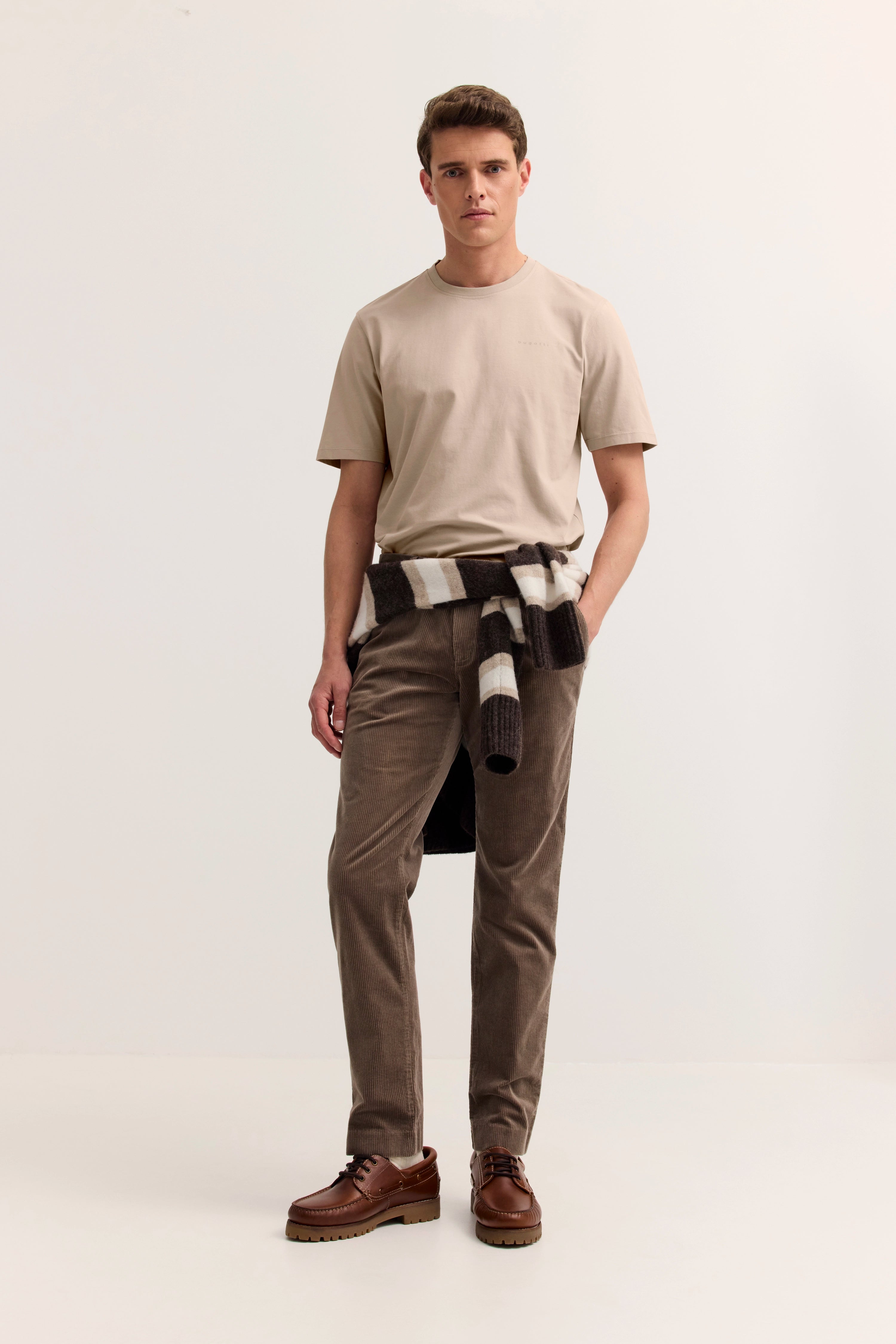 Model in beigefarbenem T-Shirt, brauner Hose, gestreiftem Schal, lässig, bugatti Stil.