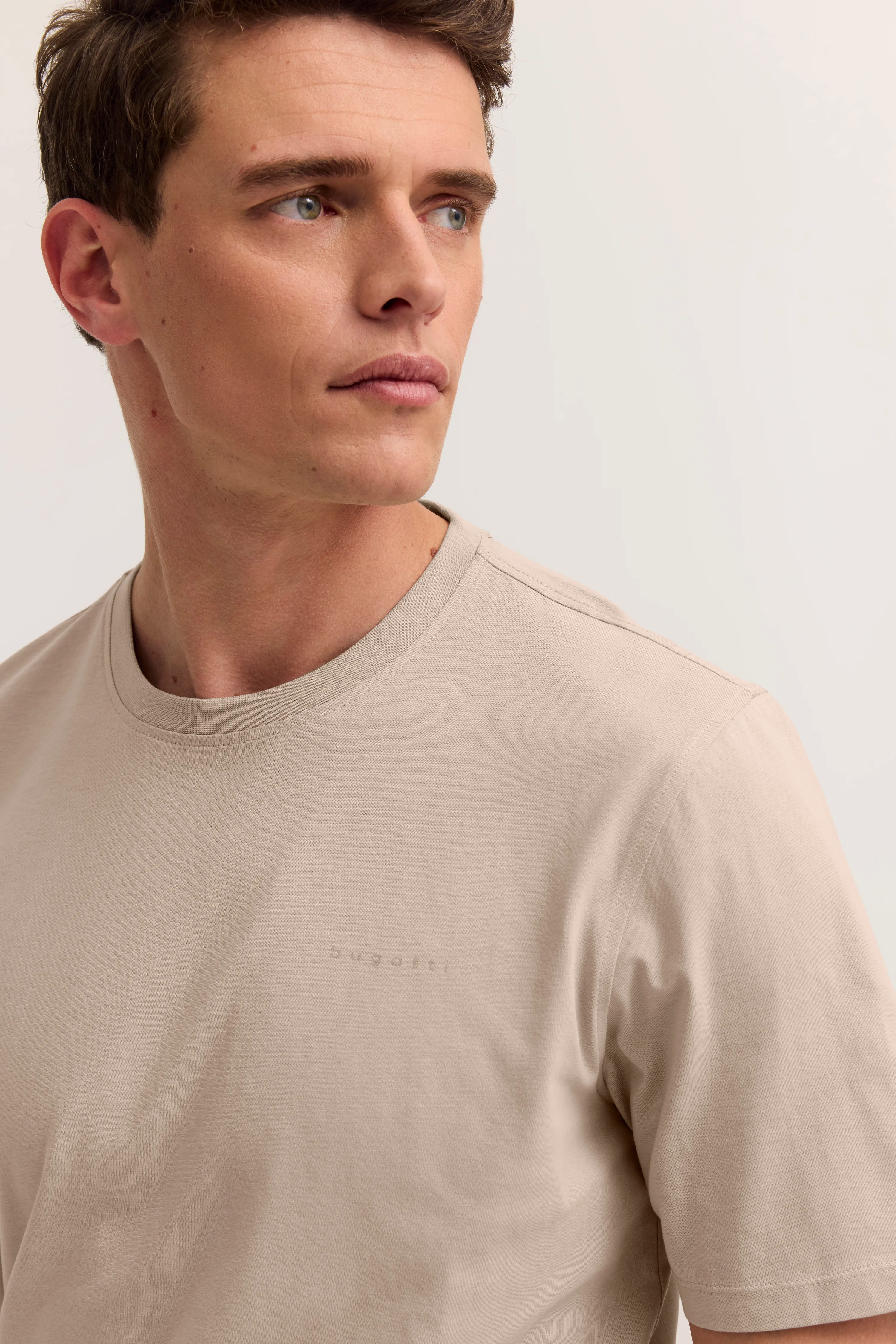 Modelbild in beigem bugatti T-Shirt, entspannter Blick zur Seite.
