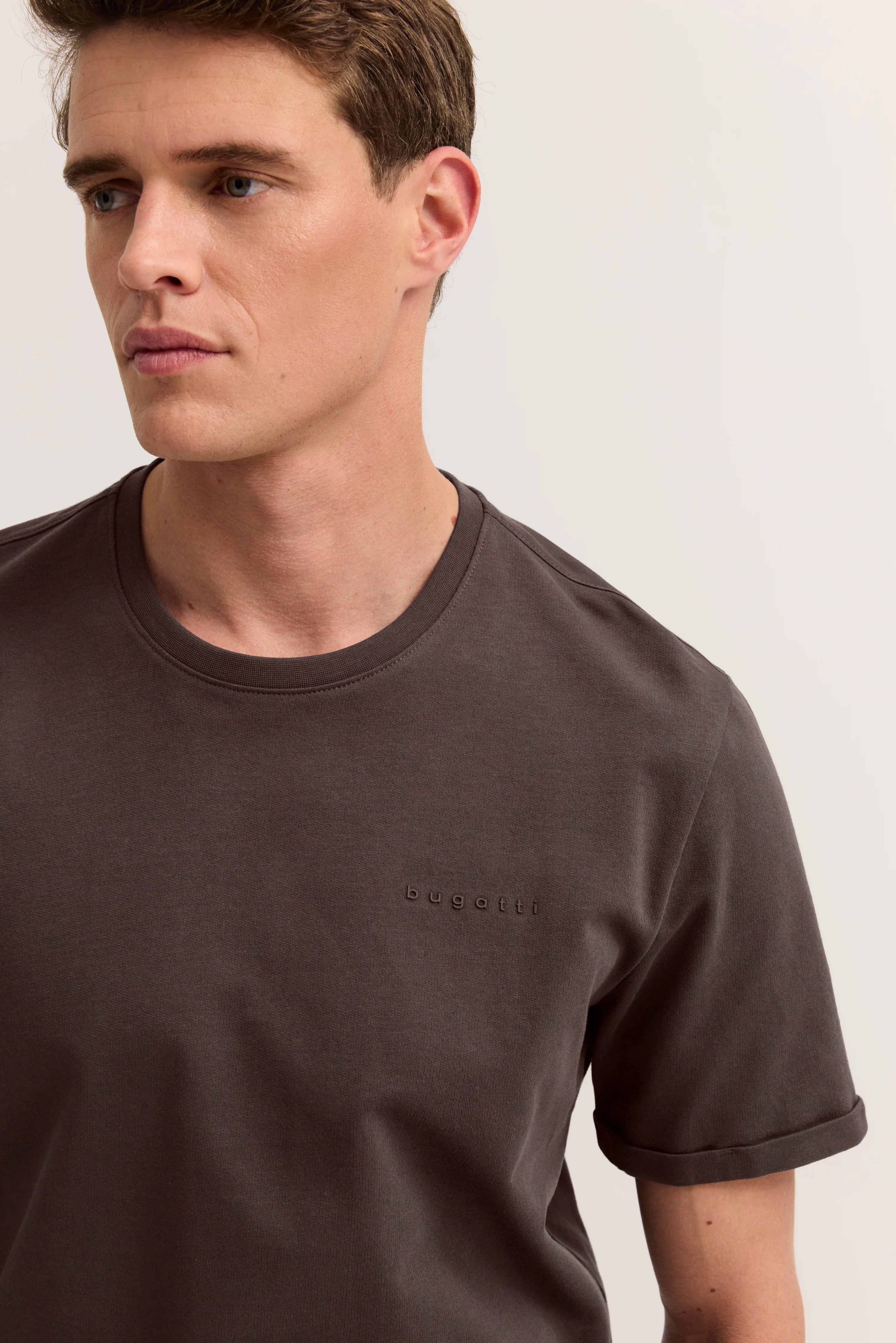 Herrenoutfit von hinten: braunes T-Shirt, beige Chinos. Modelbild, entspannte Pose.