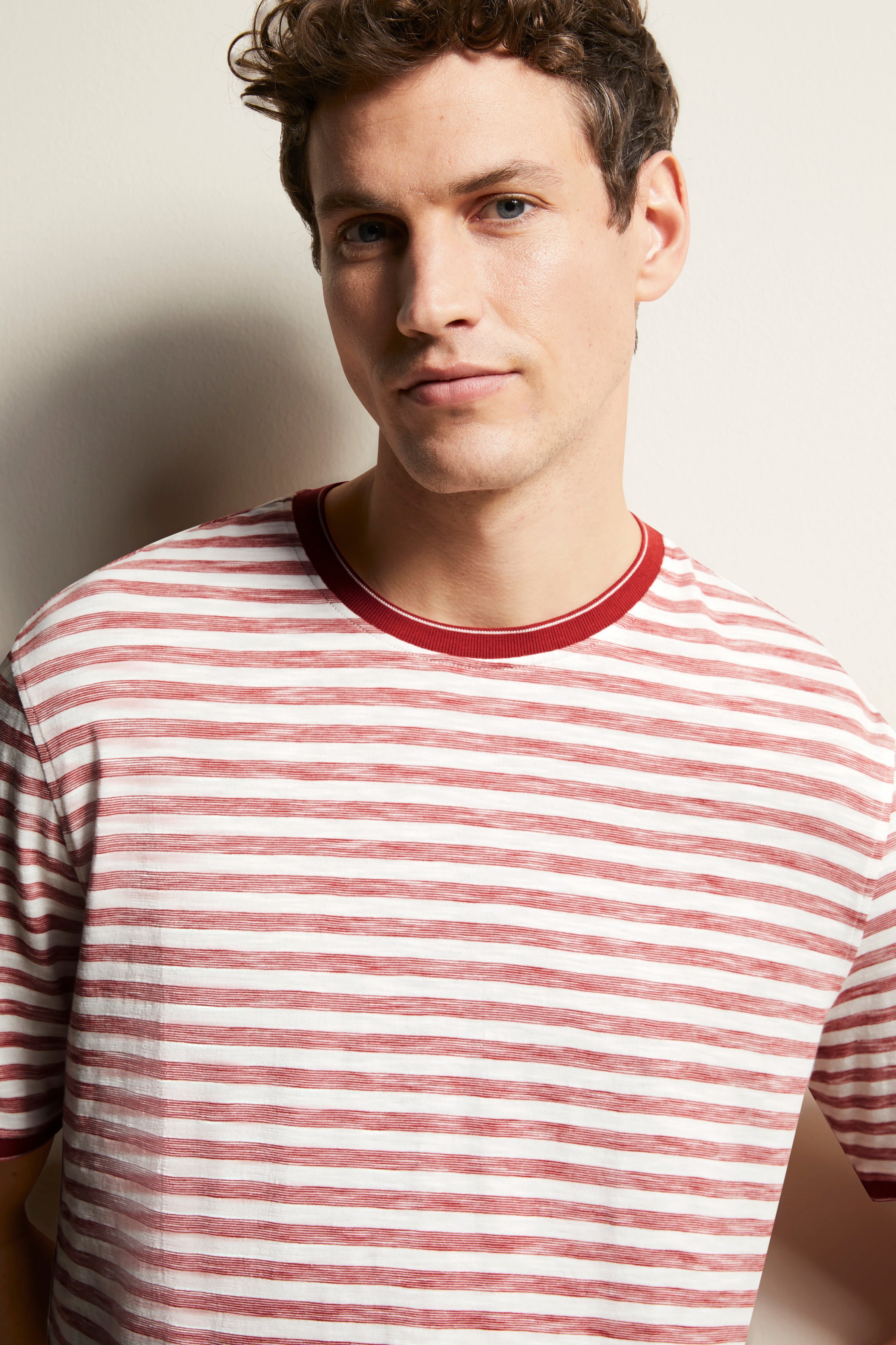 Model in red-white striped bugatti T-shirt, casual pose, relaxed expression.