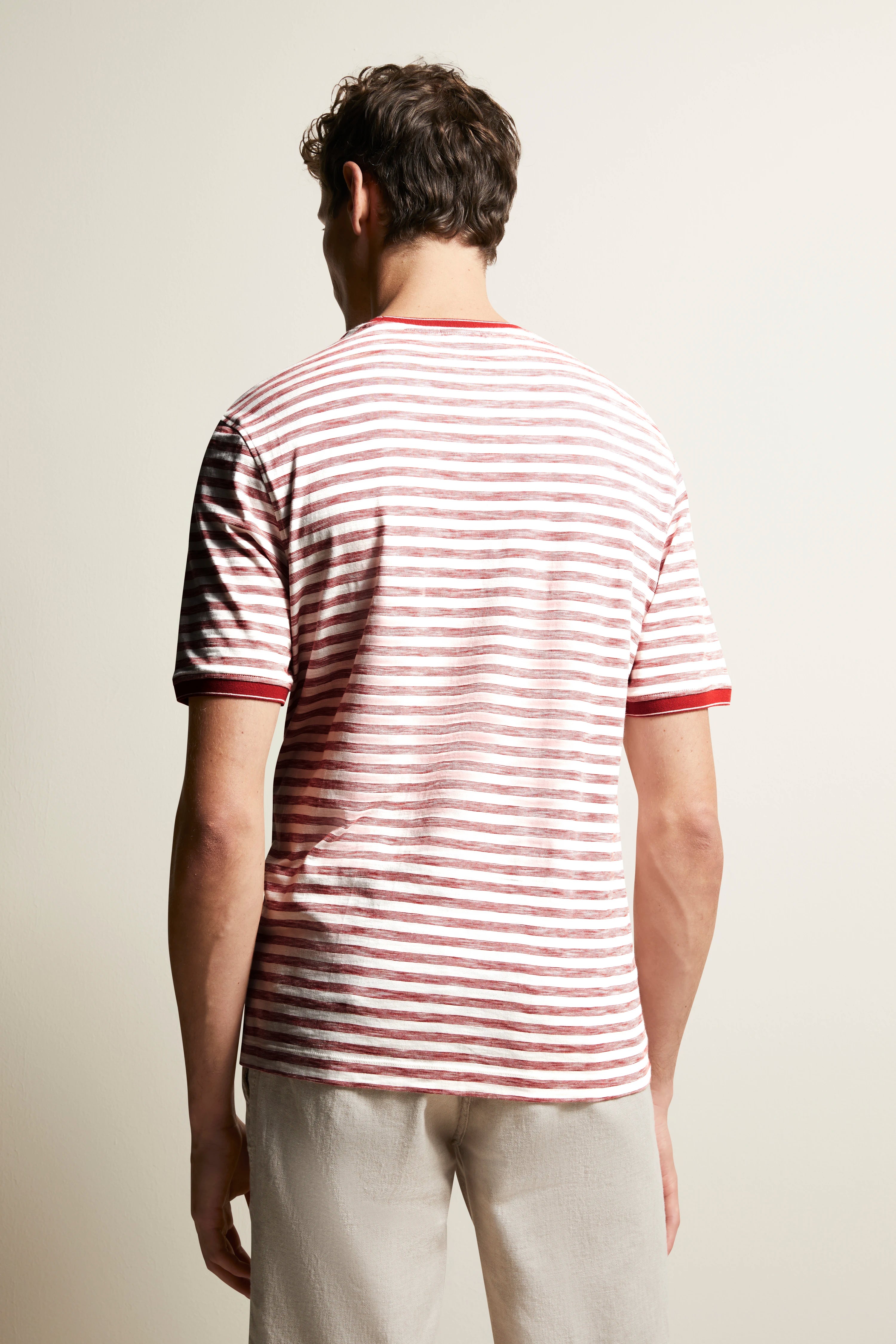 Back view of model in red-white striped bugatti T-shirt, casual beige pants, relaxed pose.