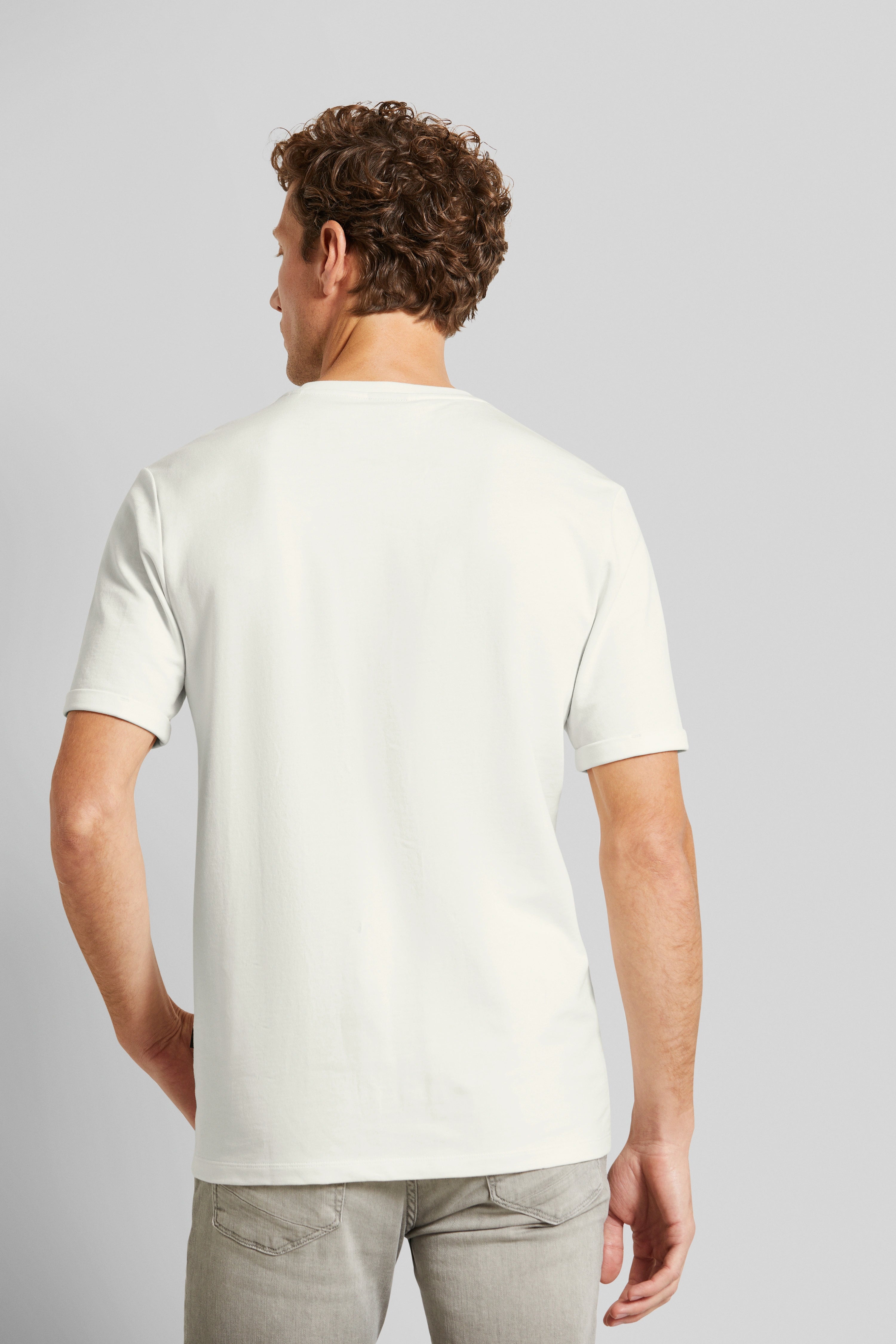Model in white bugatti T-shirt and gray jeans, back view, casual pose.