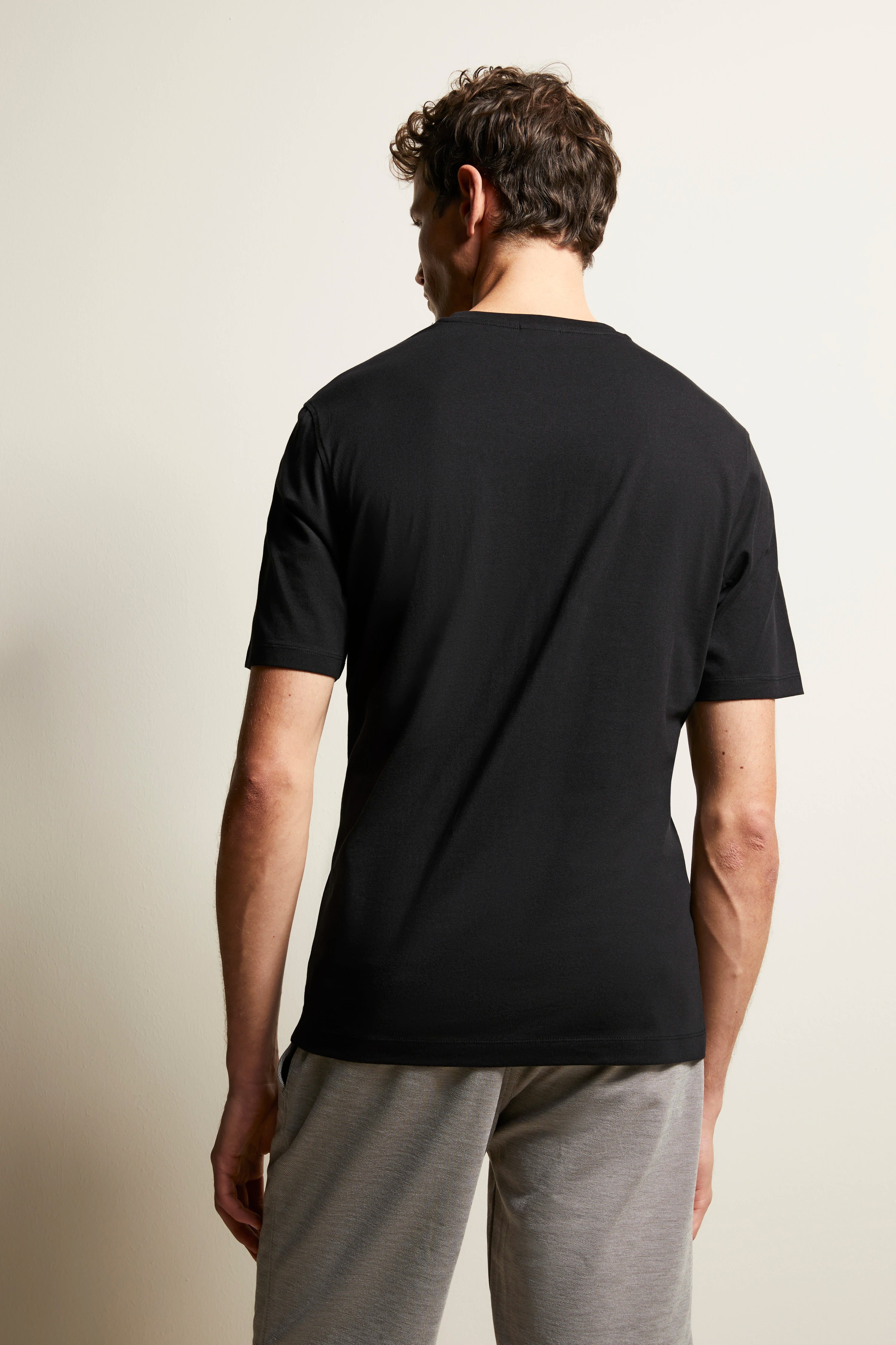 Schwarzes T-Shirt und graue Hose, Model von hinten, entspanntes Posing.
