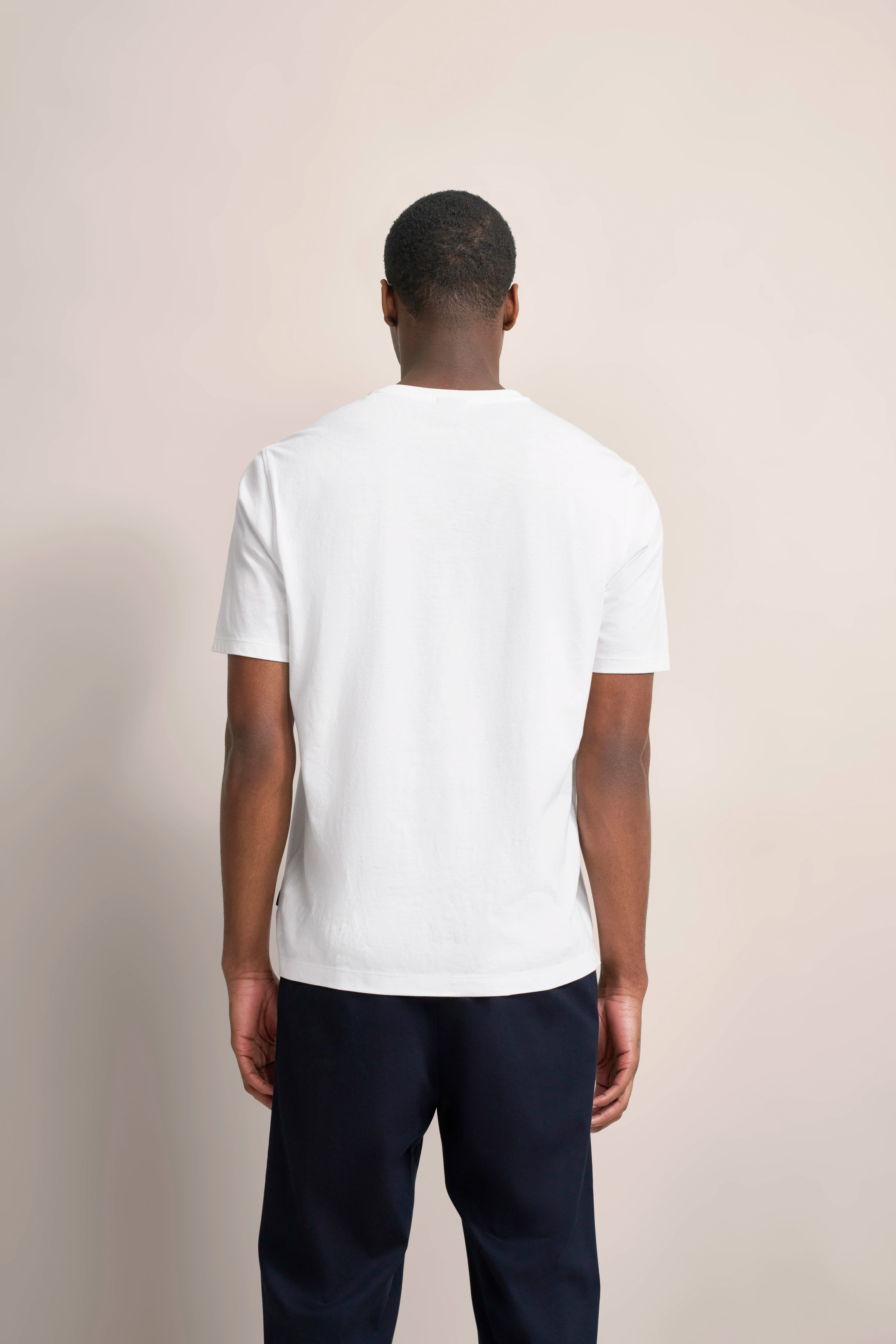 Weißes T-Shirt und dunkelblaue Hose, Modelbild von hinten, schlichtes Posing.