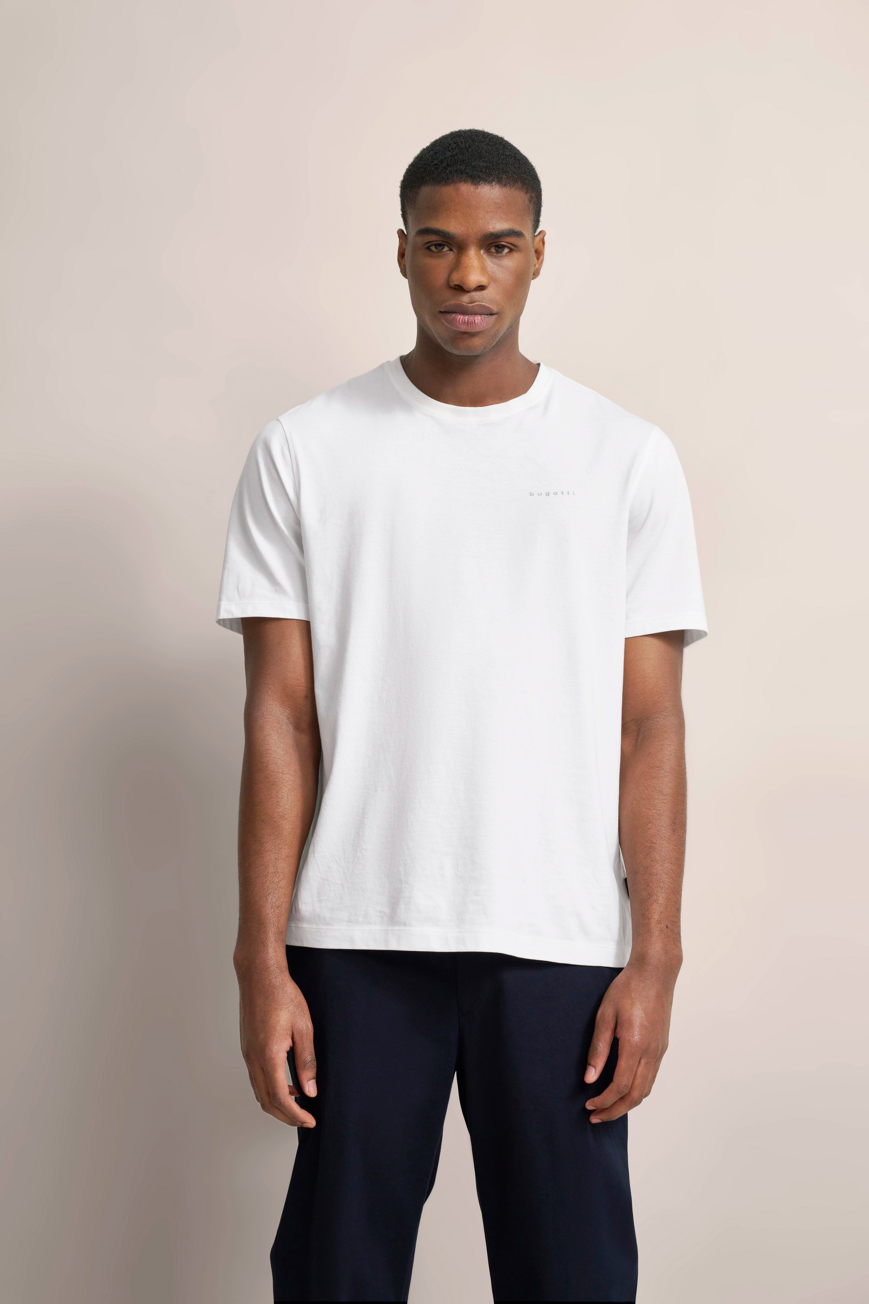 Weiße bugatti T-Shirt auf Model, legeres Posing, kombiniert mit dunklen Hosen.