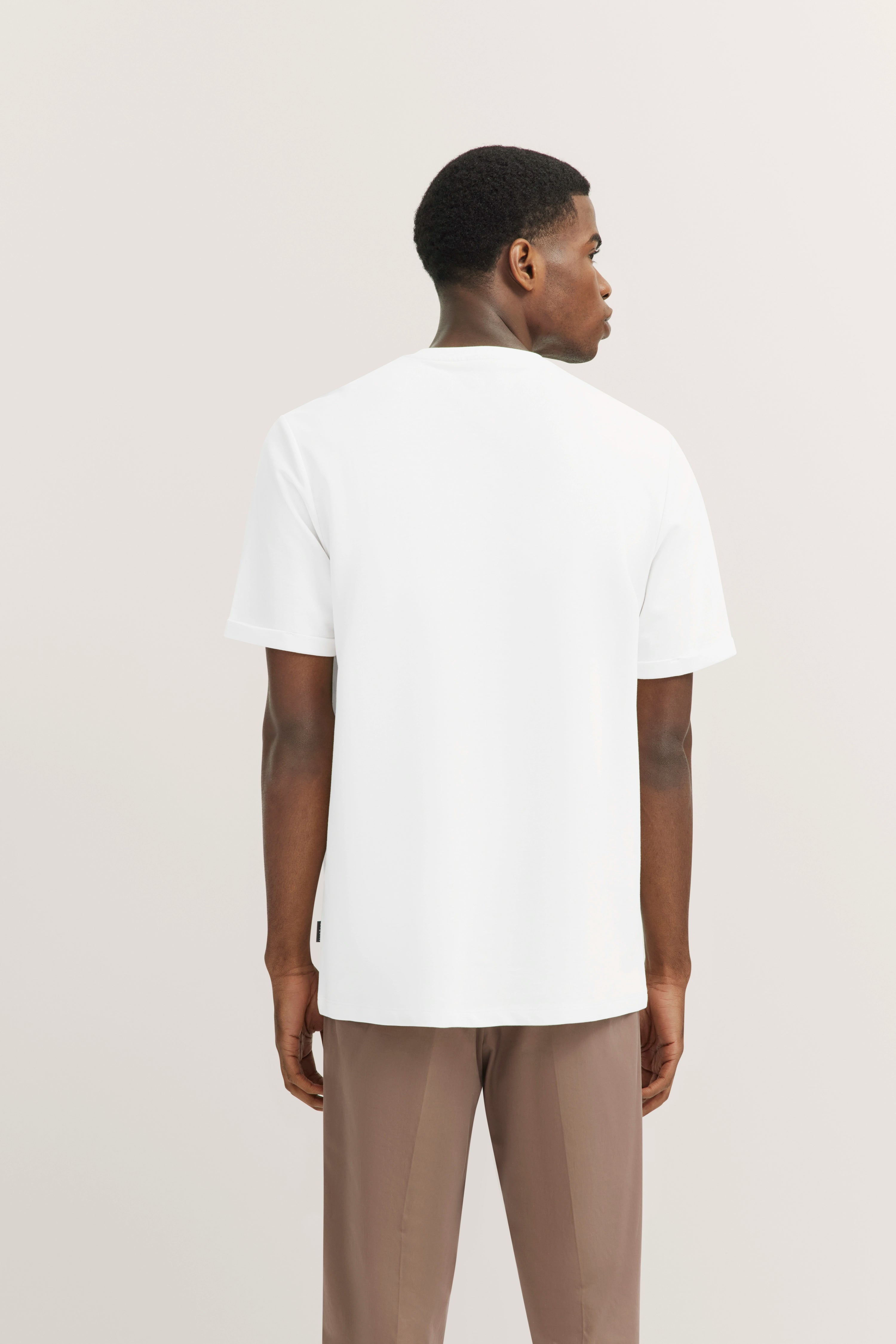 White T-shirt and beige pants, model showing back view, relaxed pose by bugatti.